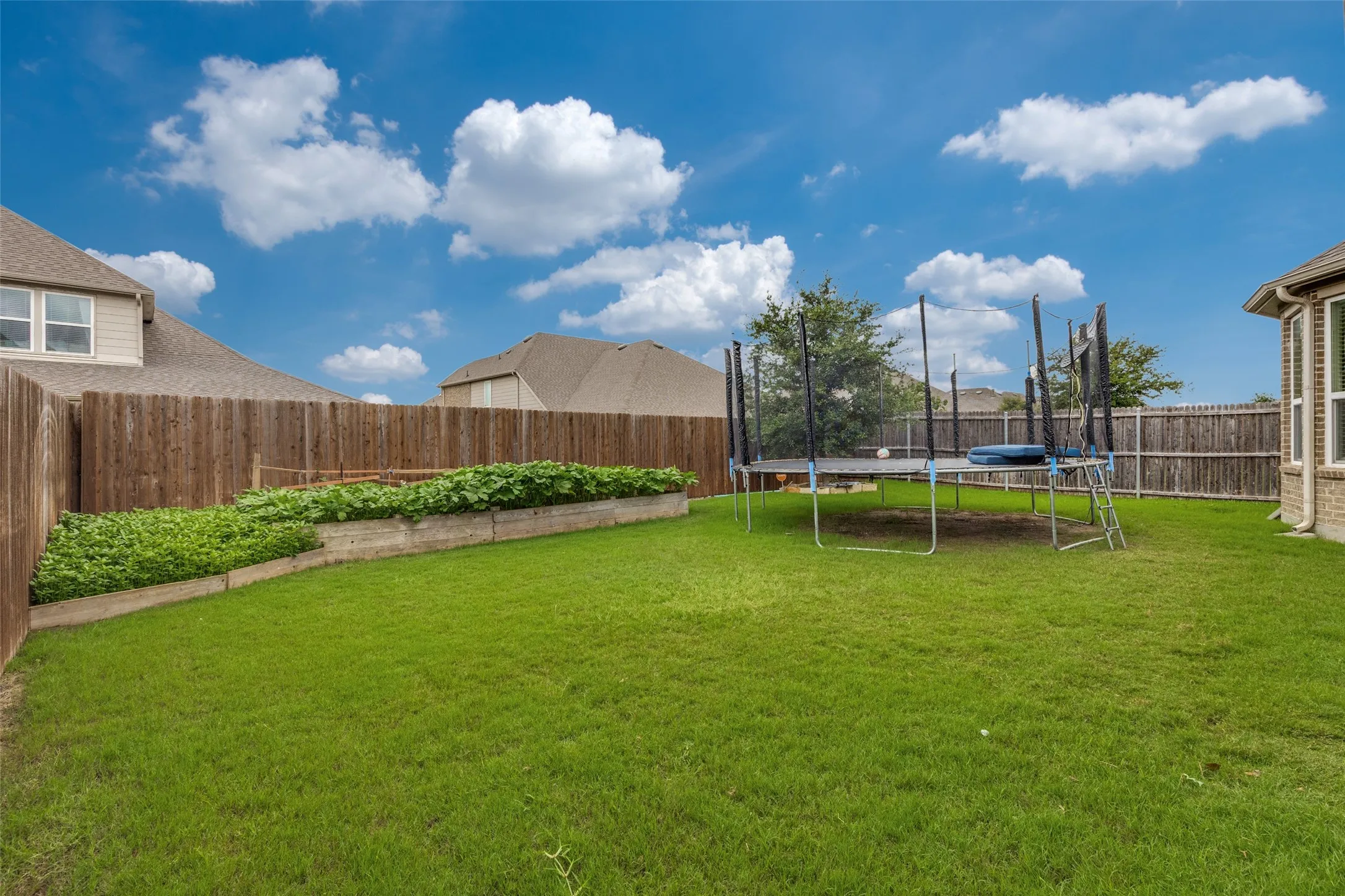 Expansive rear lawn featuring a wooden privacy fence and a raised garden bed with established plantings