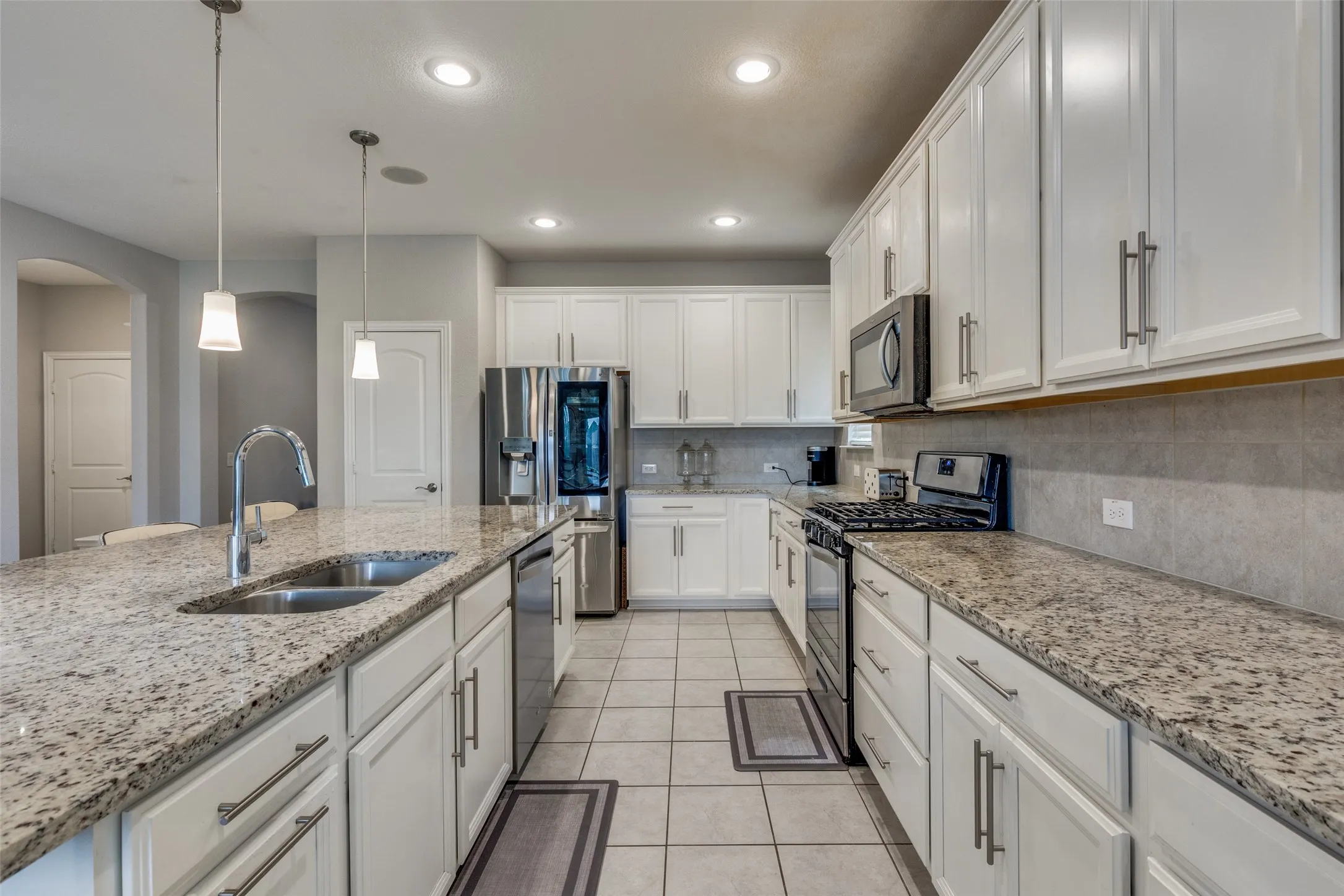 Spacious kitchen featuring an expansive island with a double basin sink, light-toned cabinetry, granite countertops, stainless steel appliances, and recessed lighting