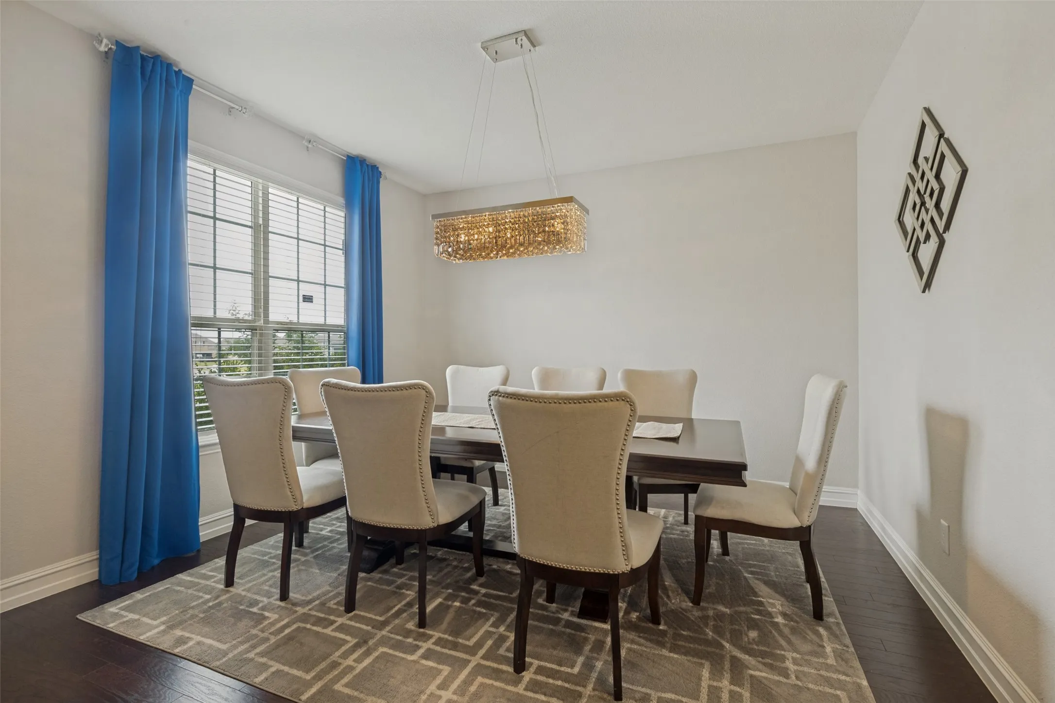 Spacious dining area featuring dark wood-finish flooring, a large window with blinds, and white baseboards