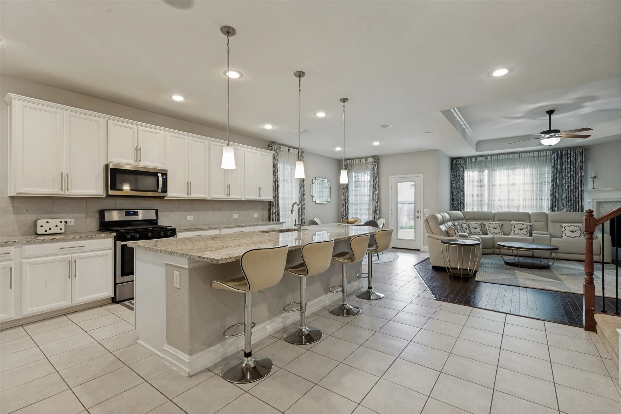 Open-concept living area featuring a kitchen island with pendant lighting, stainless steel appliances, white cabinetry, and granite countertops
