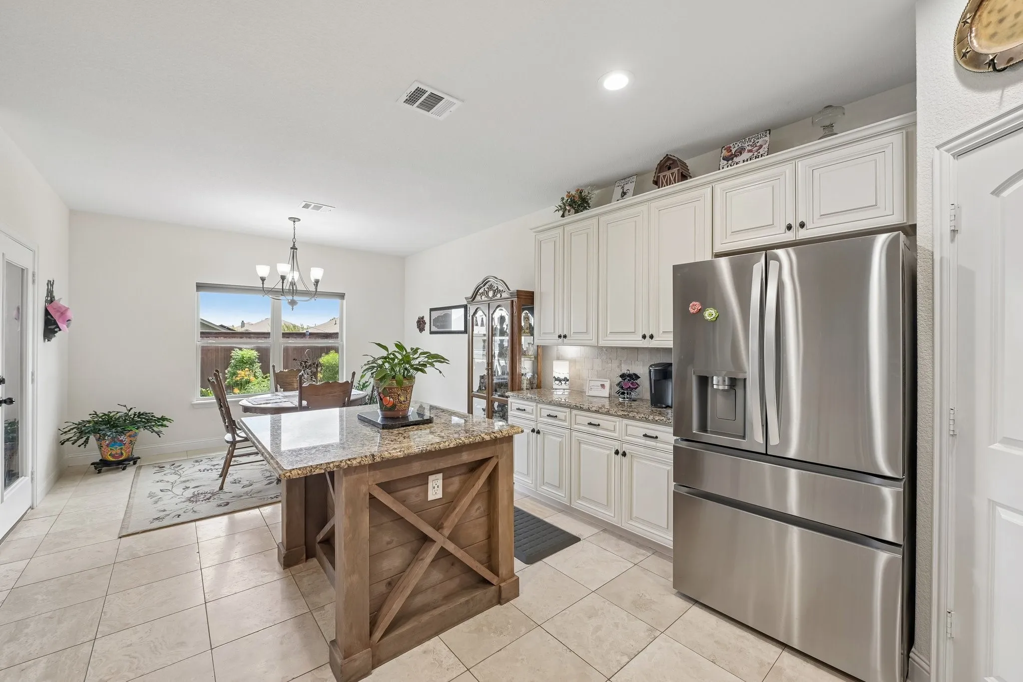 Kitchen featuring a central island with a granite countertop, wood-finish base, stainless steel refrigerator, white cabinetry, and tile flooring