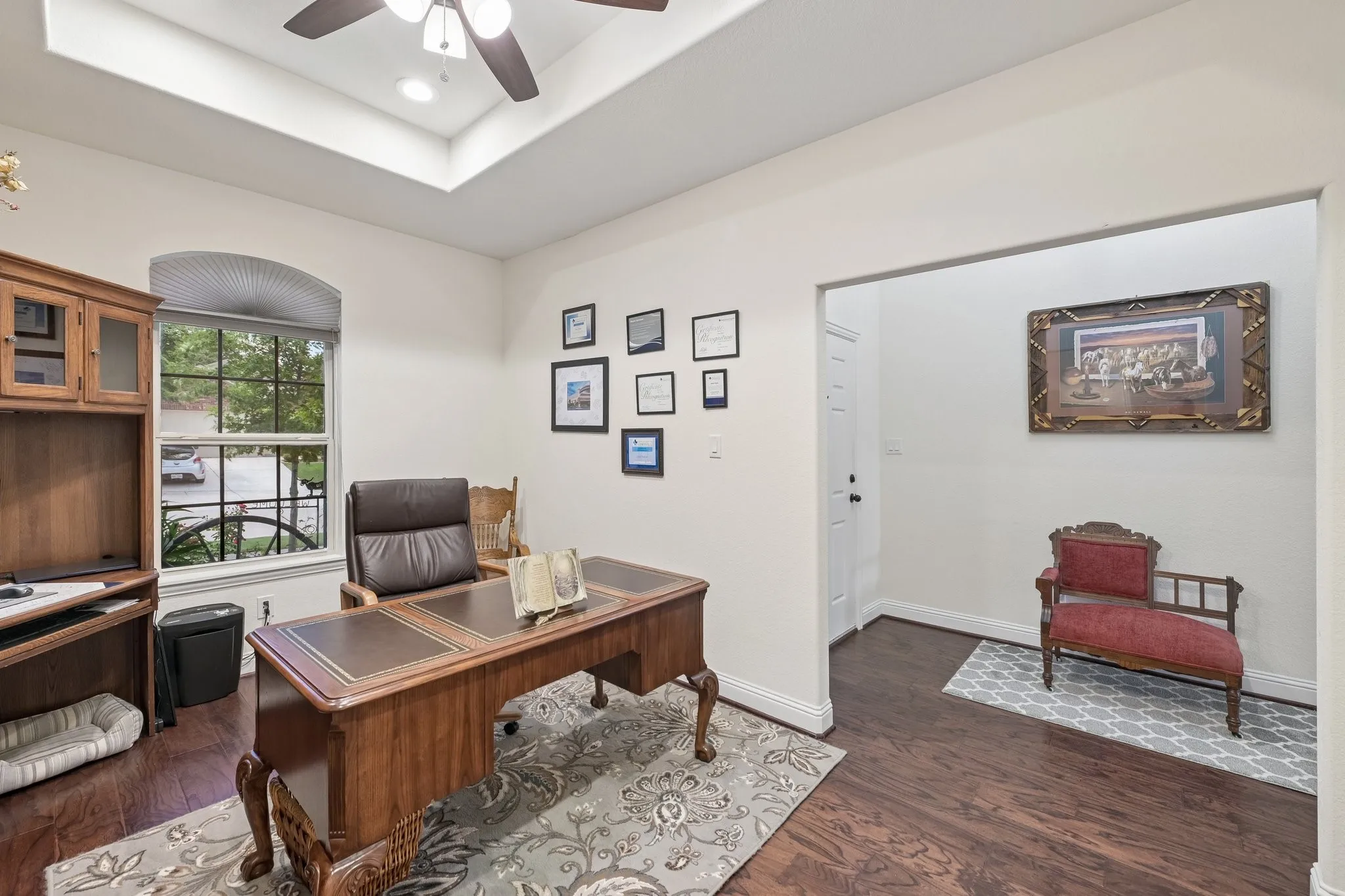 Dedicated office space featuring wood-finish flooring, a tray ceiling with a ceiling fan, and an arched window