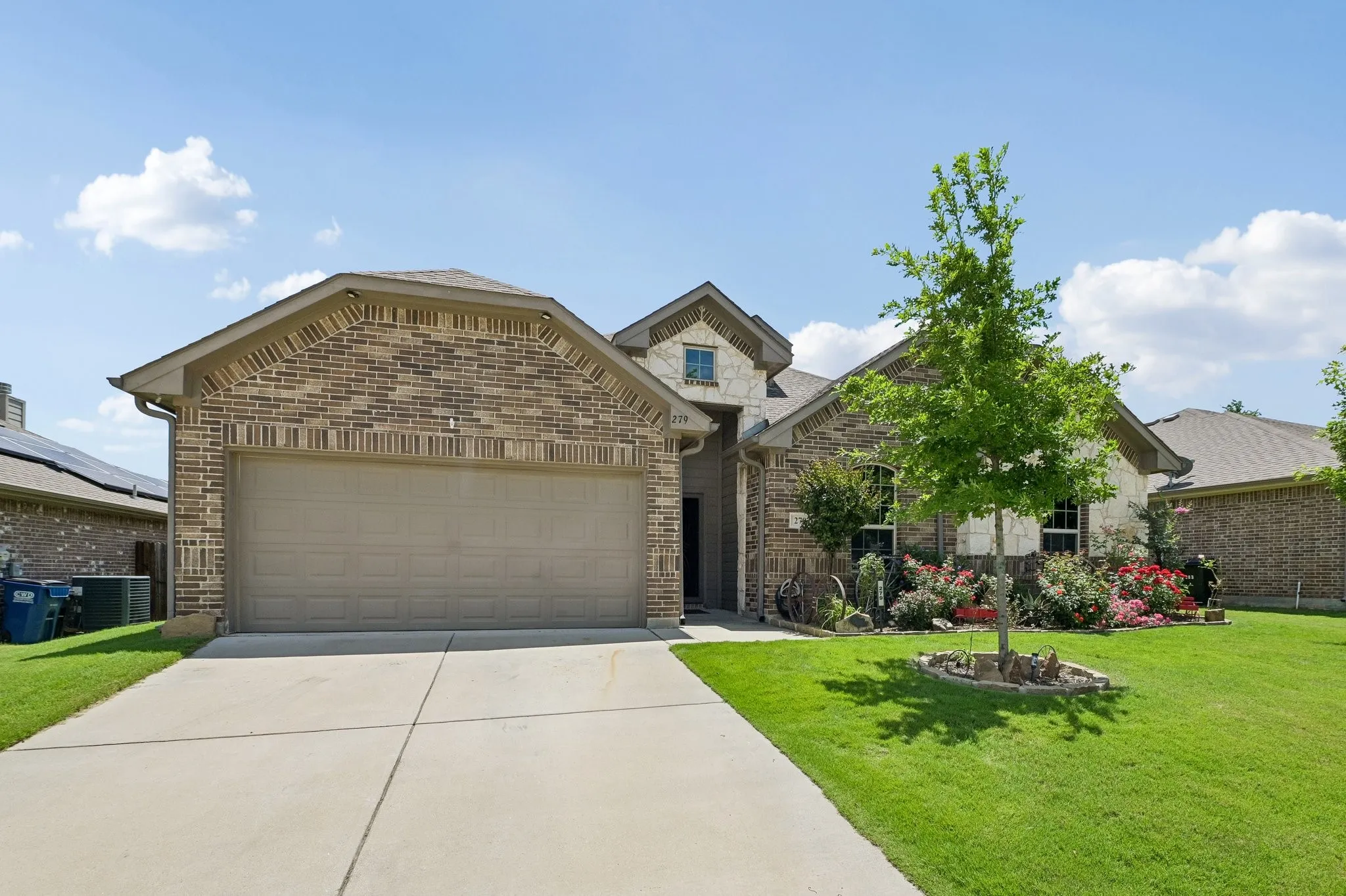 Brick and stone exterior featuring a two-car garage, concrete driveway, and a front lawn with mature landscaping