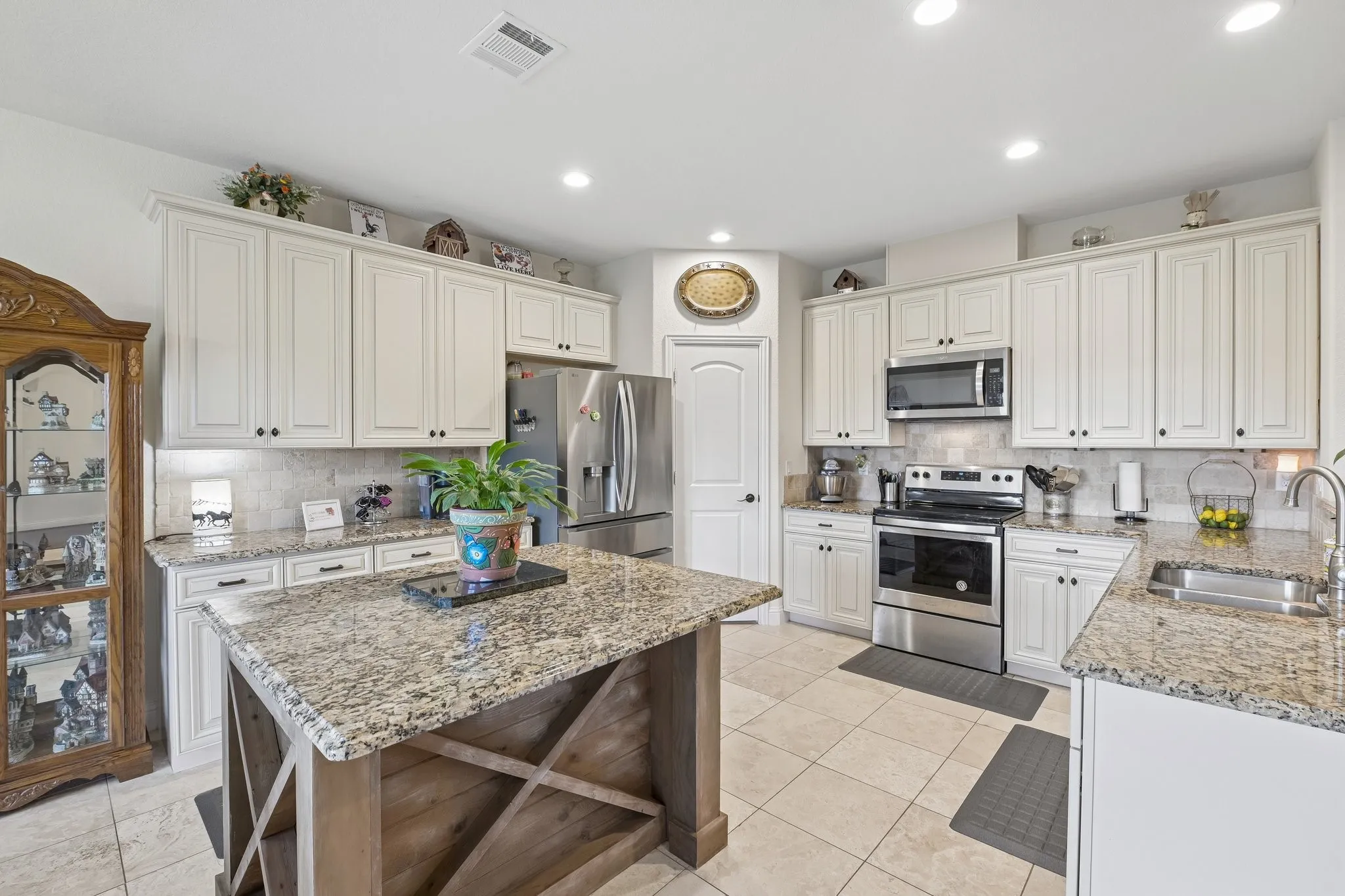 Spacious kitchen featuring an island with a wood-finish base and stone countertop, white cabinetry with dark hardware, stainless steel appliances, recessed lighting, and tile flooring