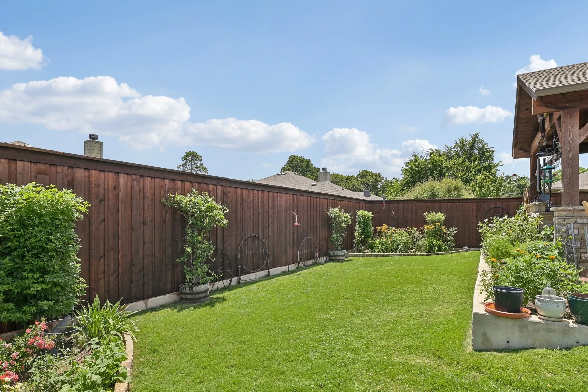 Expansive backyard featuring a manicured lawn, established garden beds, and a perimeter wood fence