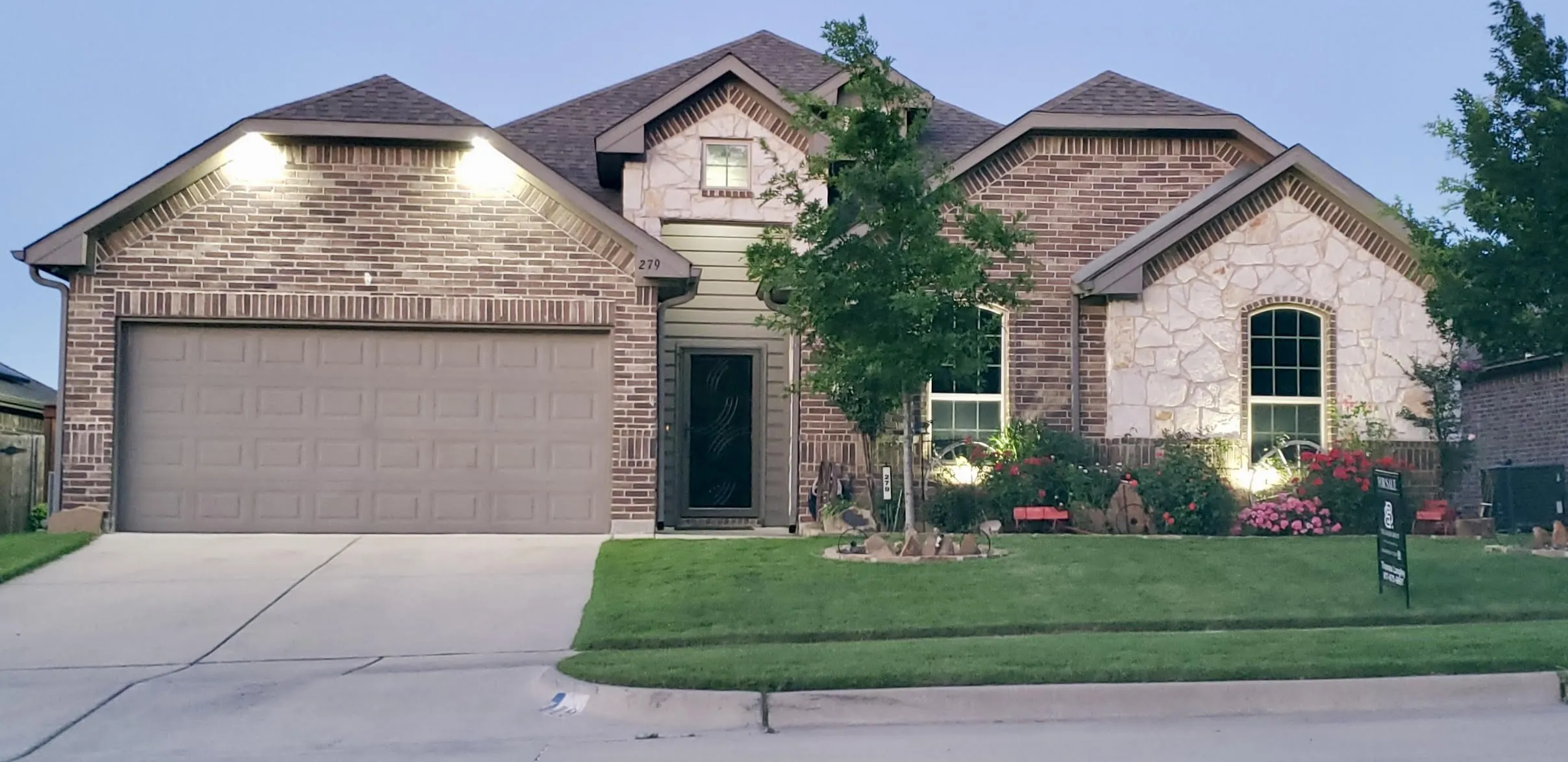 Brick and stone exterior featuring a two-car garage, manicured lawn, and established landscaping