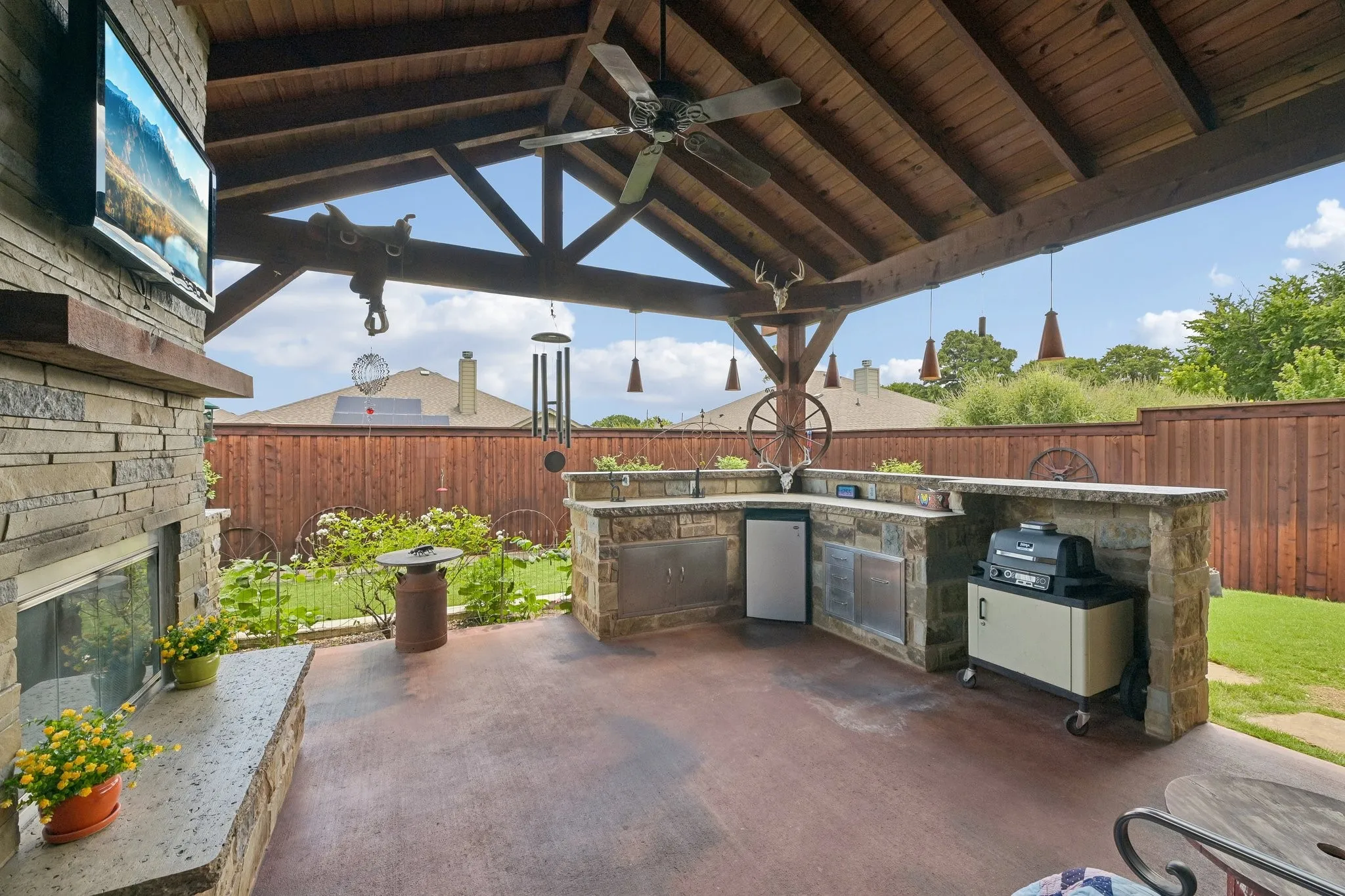 Covered patio with a stone-clad outdoor kitchen featuring a built-in grill and refrigerator
