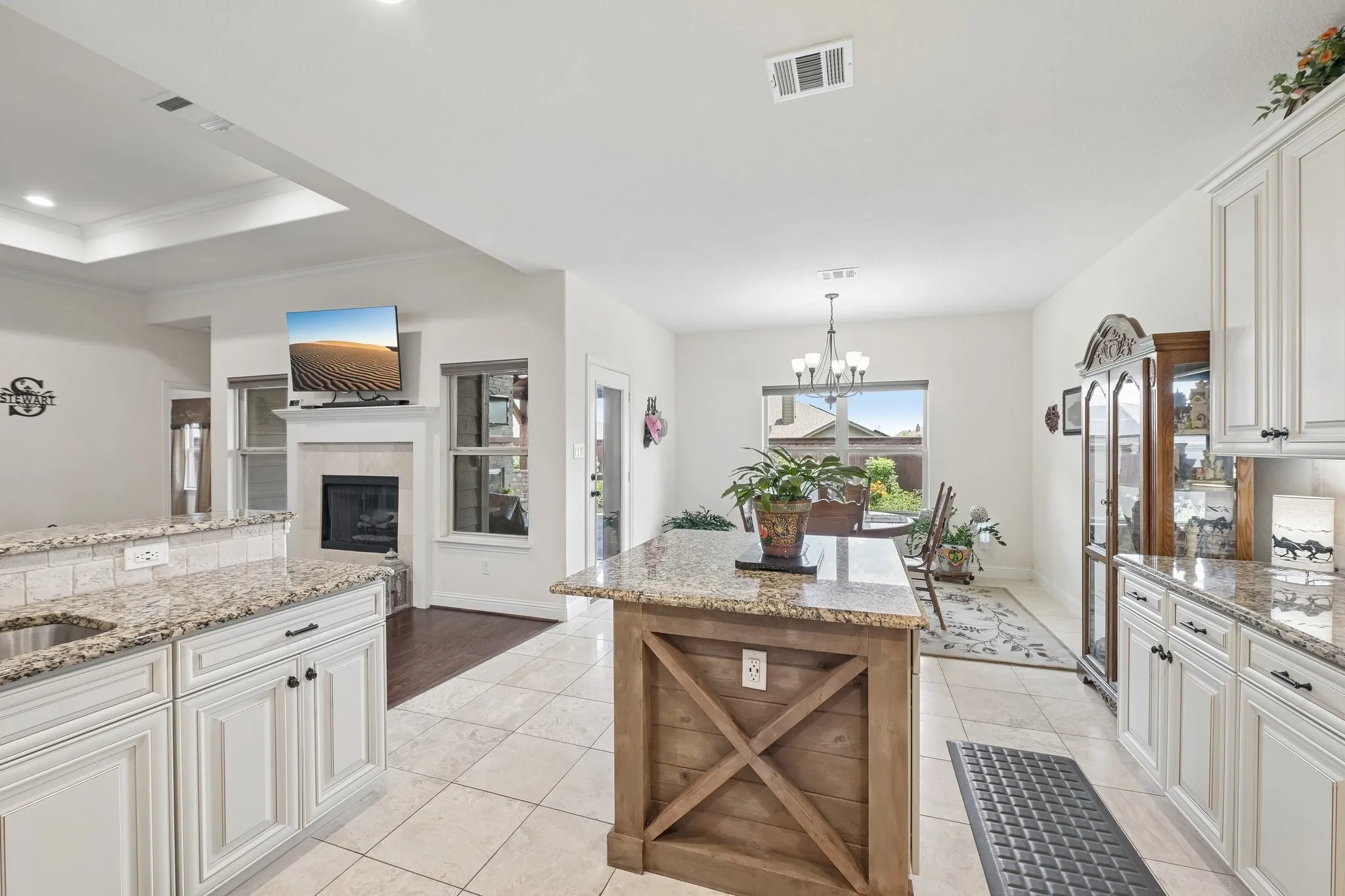 Spacious kitchen featuring white cabinetry, granite countertops, tile flooring, a large island with wood-finish paneling, and an integrated stainless steel sink