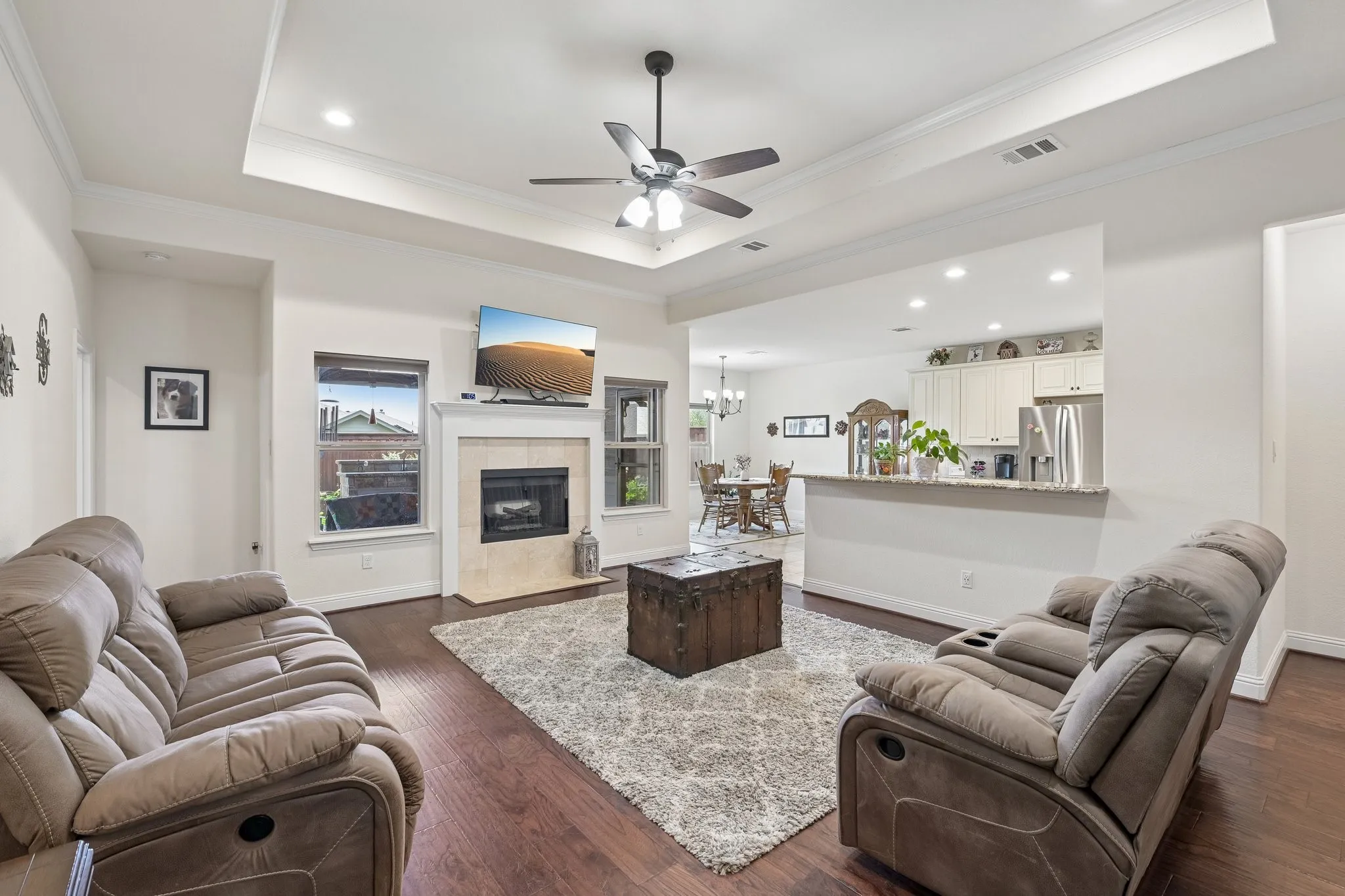 Spacious living area featuring rich wood-finish flooring and a tray ceiling with a ceiling fan