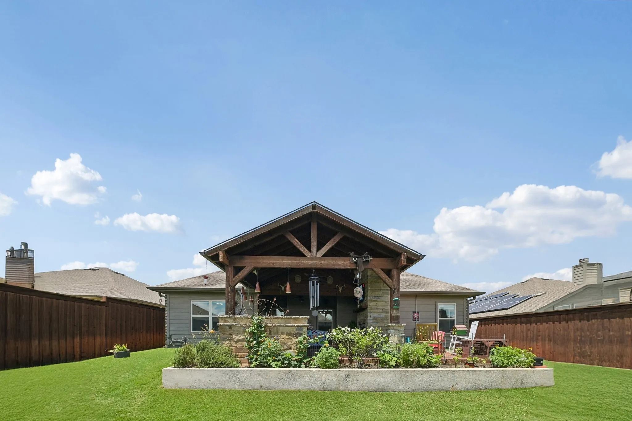 Expansive backyard featuring a covered patio with exposed wood beams, stone accents, and a built-in planter box