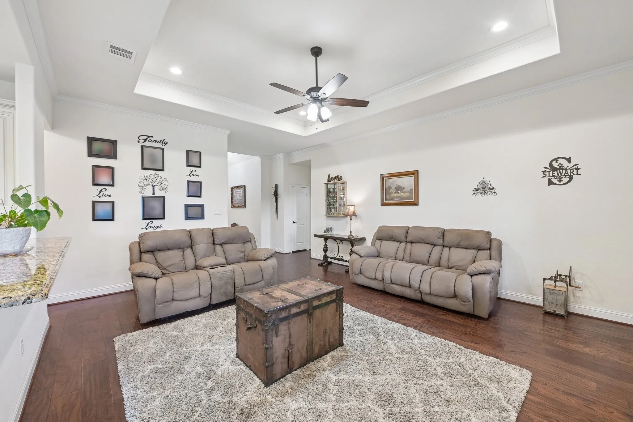 Spacious living area featuring wood-finish flooring, a tray ceiling with recessed lighting and a ceiling fan, and white baseboards