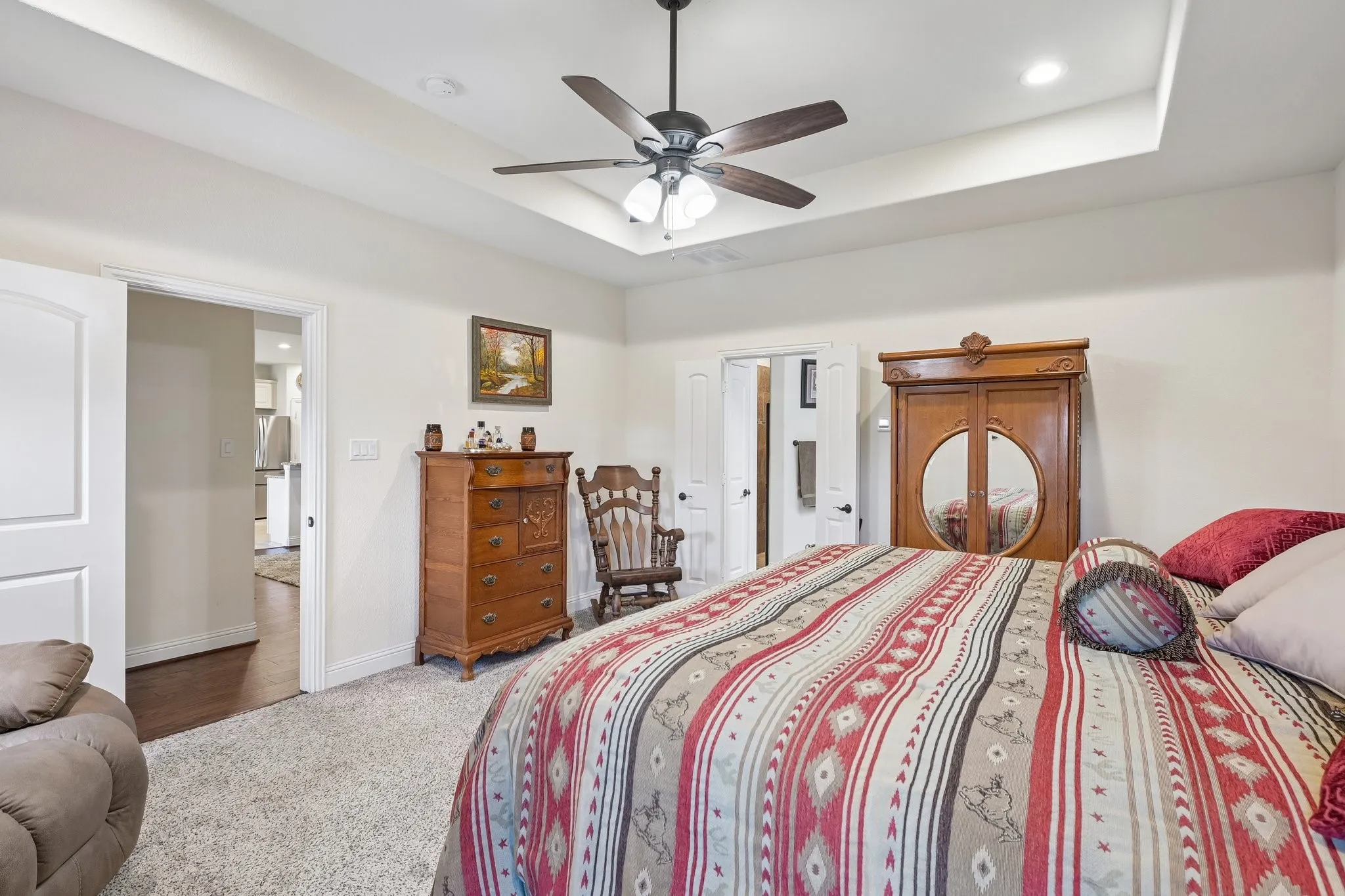 Spacious bedroom featuring a recessed tray ceiling, ceiling fan, and light-toned carpeting