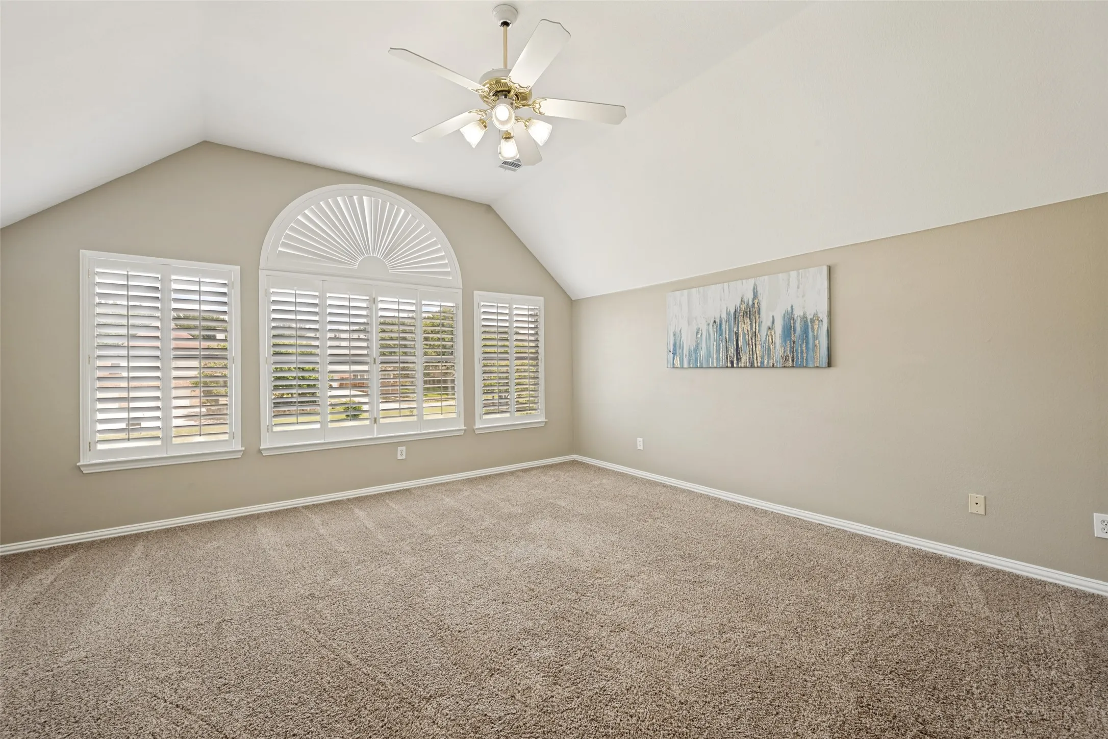 Vaulted ceiling room featuring three arched-top windows with white plantation shutters, a ceiling fan with light fixture, and neutral-toned carpeting