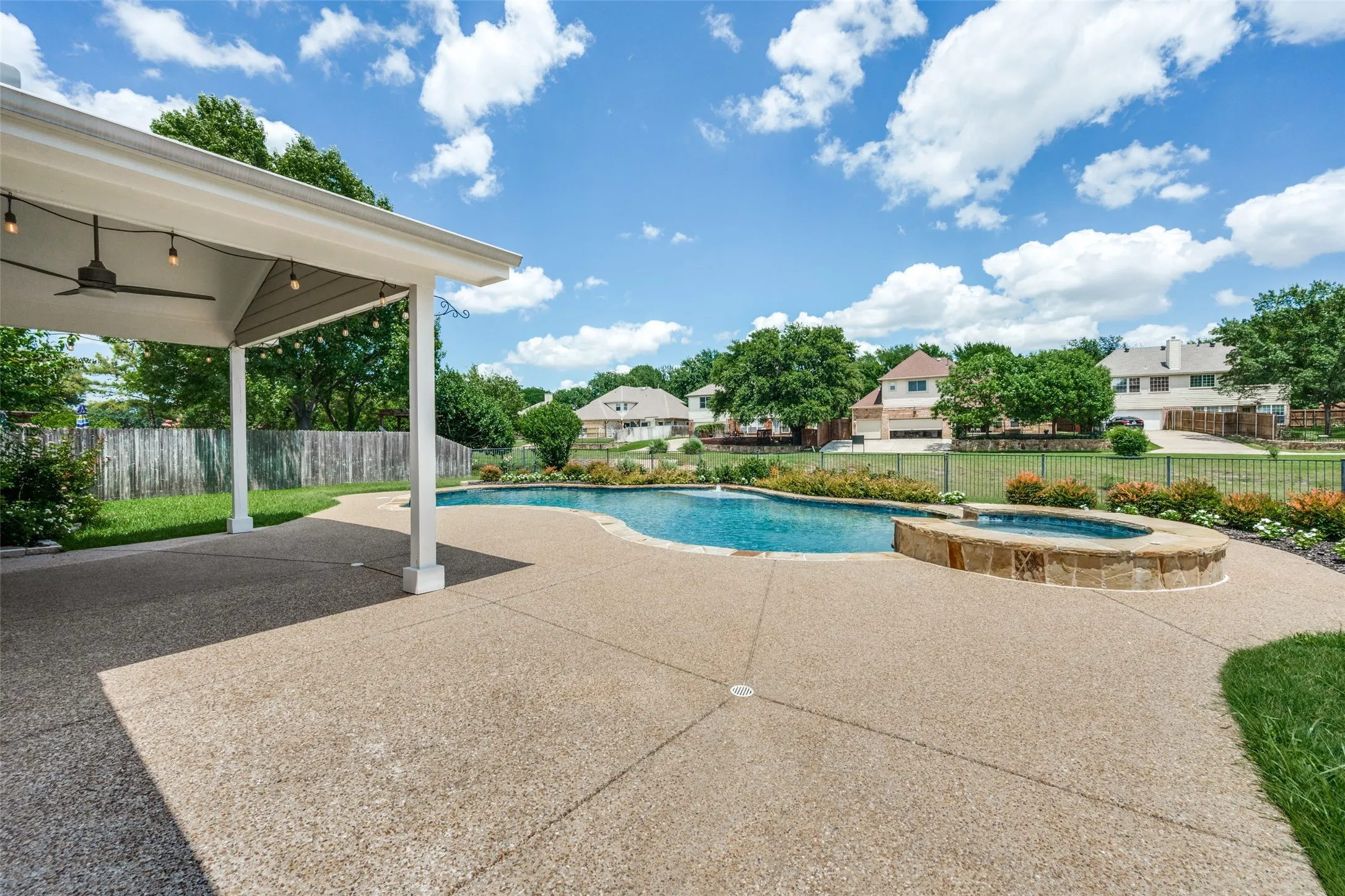 Expansive outdoor living area featuring a covered patio with ceiling fan, string lighting, a freeform swimming pool, and an integrated stone-clad spa