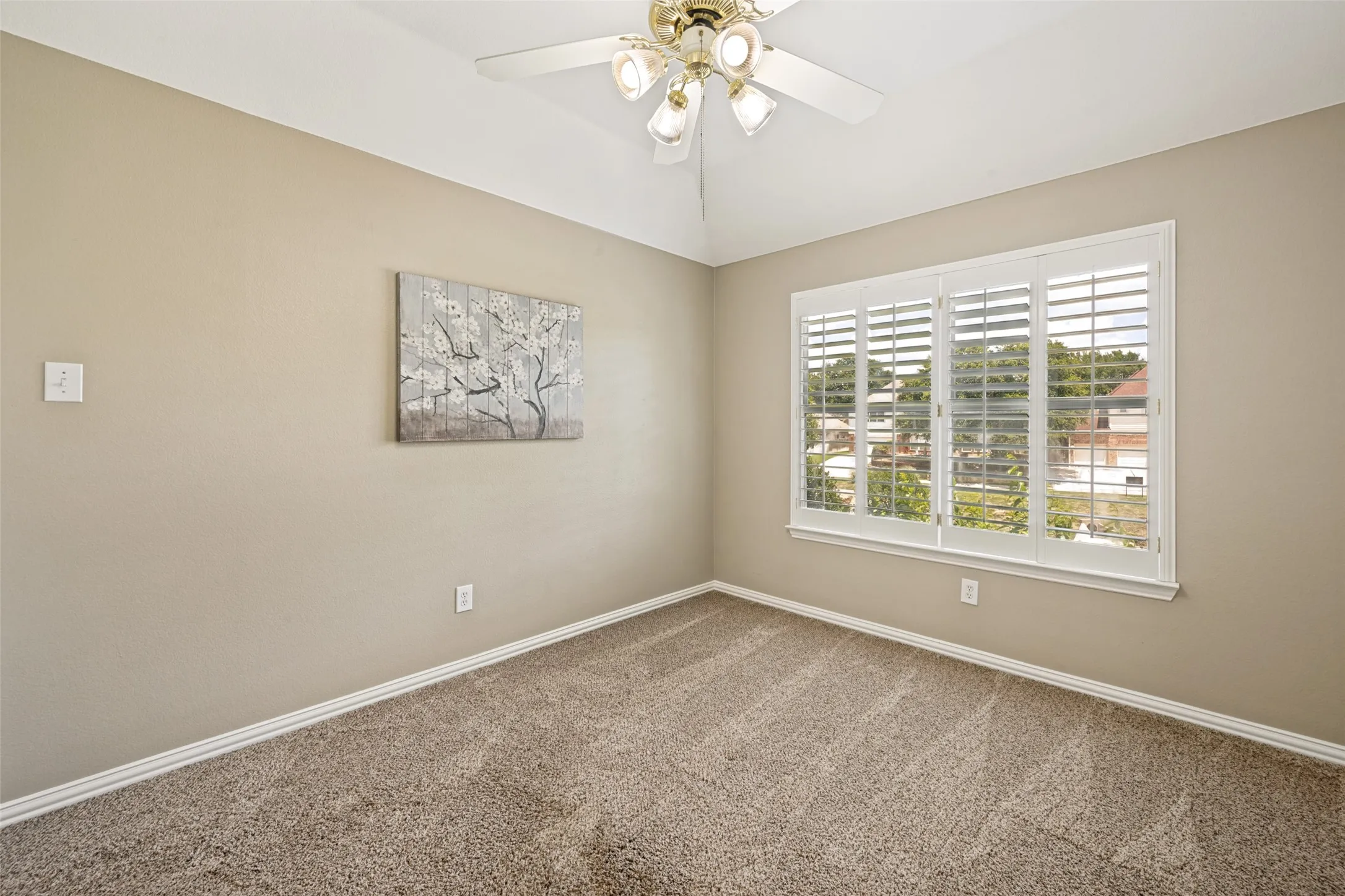 Carpeted room featuring a vaulted ceiling, ceiling fan with integrated lighting, and a window with white plantation shutters