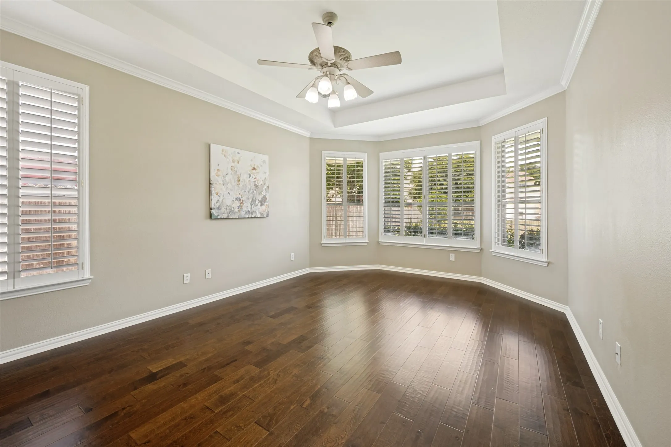 Expansive room featuring wood-finish flooring, a tray ceiling, and a ceiling fan with integrated lighting