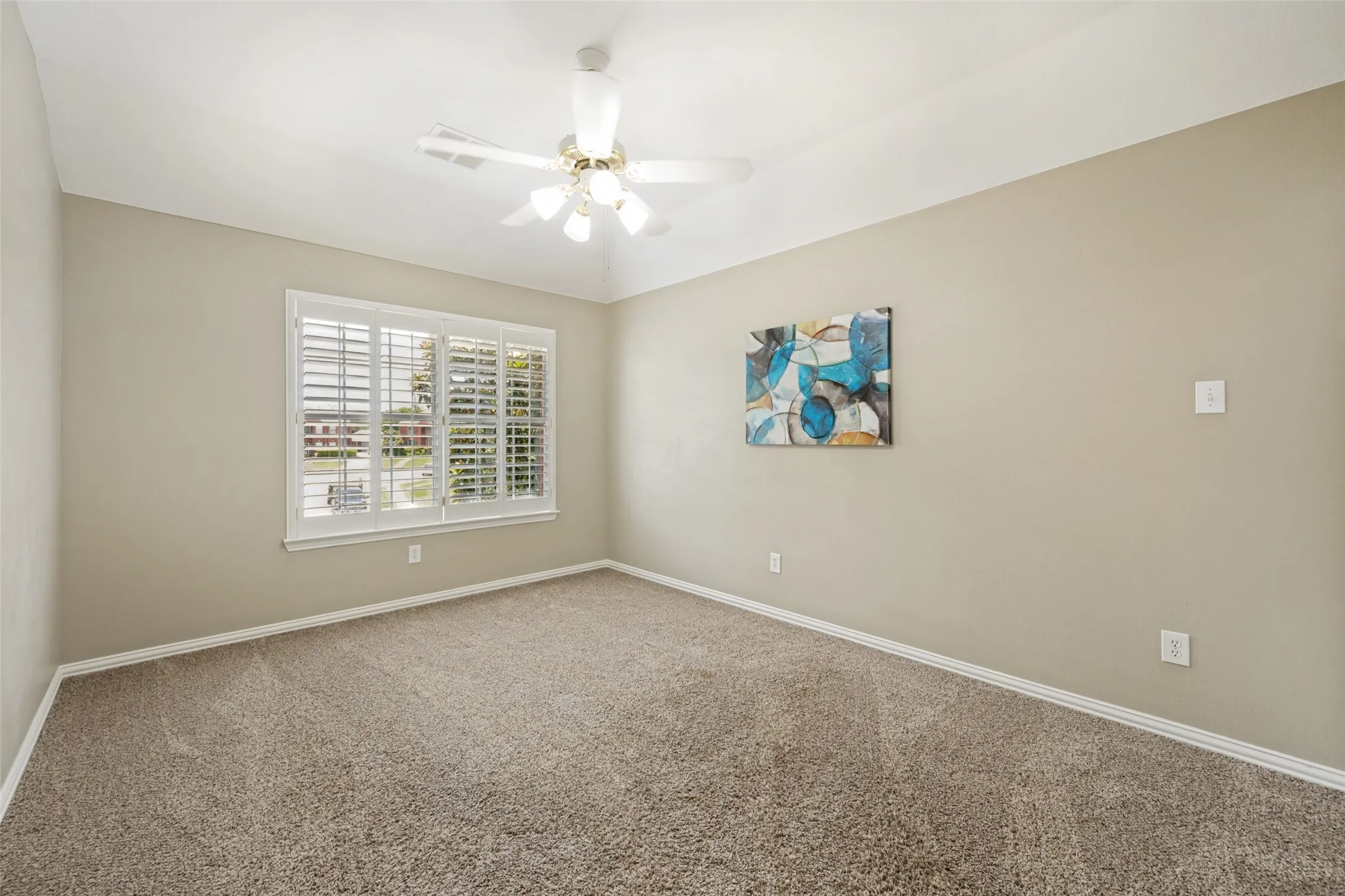 Carpeted room featuring a white ceiling fan with integrated lighting, a window with plantation shutters, light neutral wall paint, and white baseboards