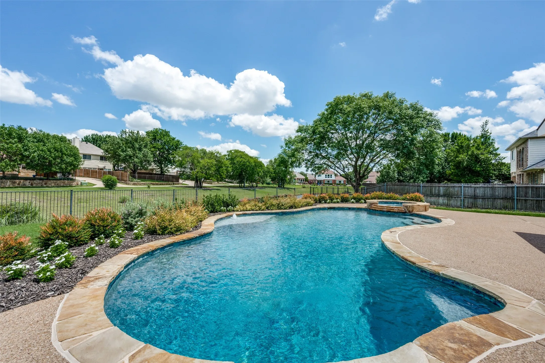 Freeform swimming pool featuring natural stone coping, an integrated spa, and an expansive aggregate concrete patio