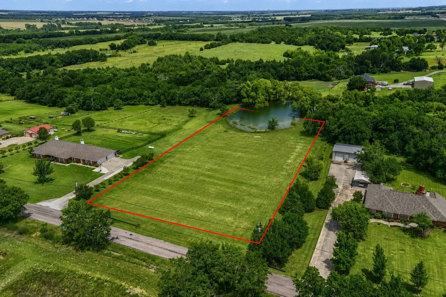 Spacious land parcel featuring a private pond, open grassy areas, and surrounding mature trees