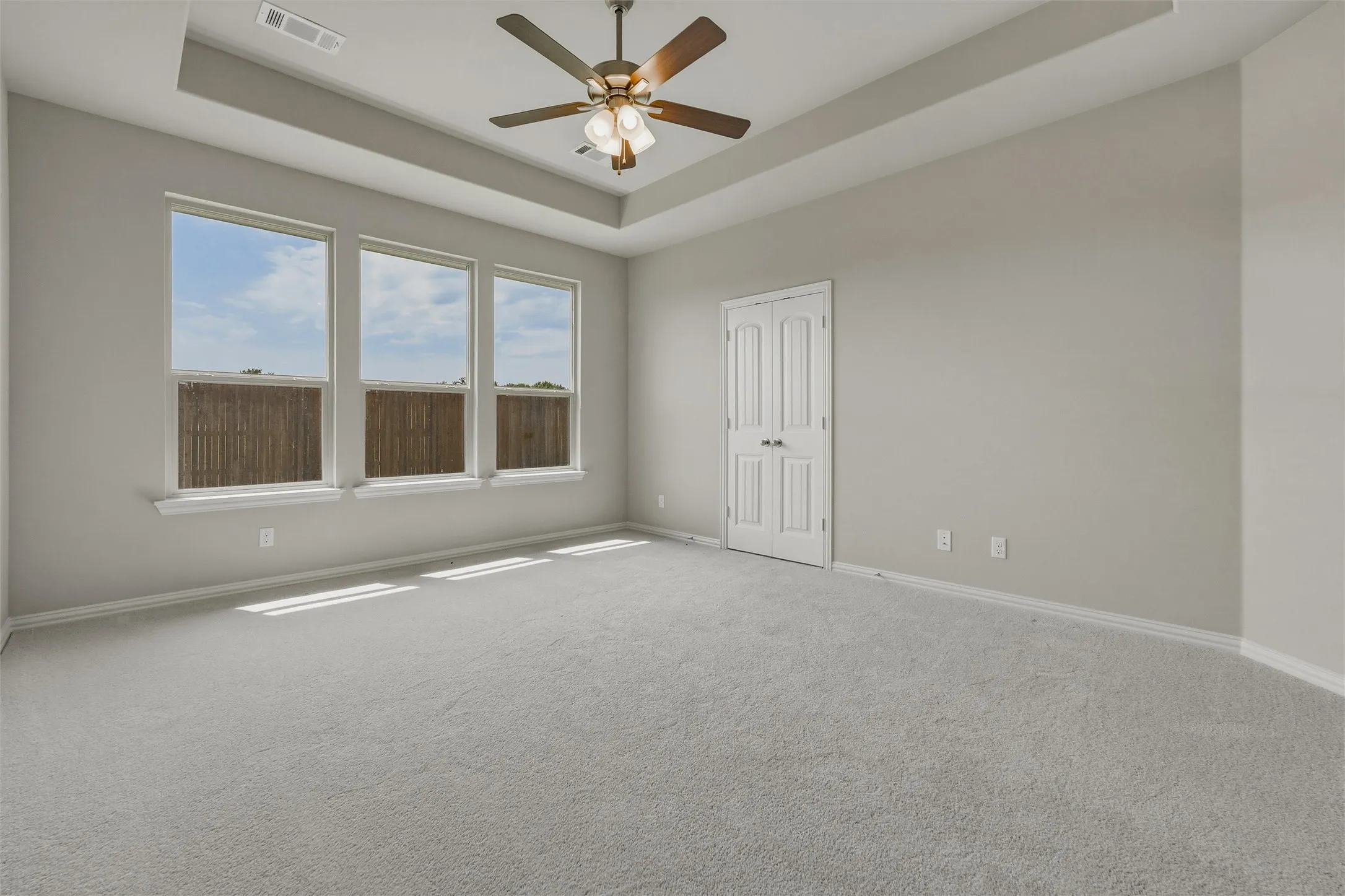 Tray ceiling with a ceiling fan, three pane windows, and light gray wall paint