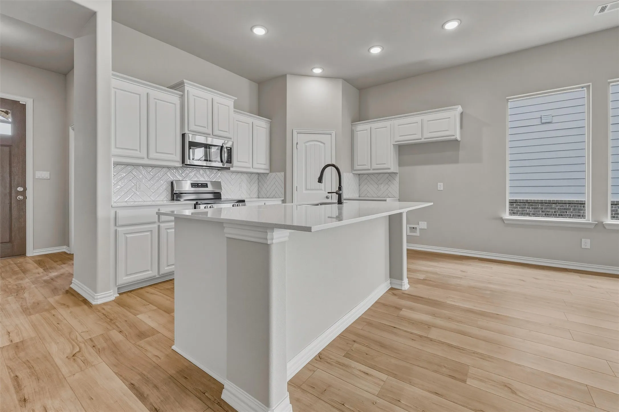 Kitchen featuring a center island, white cabinetry, integrated stainless steel appliances, a herringbone tile backsplash, and light wood-finish flooring