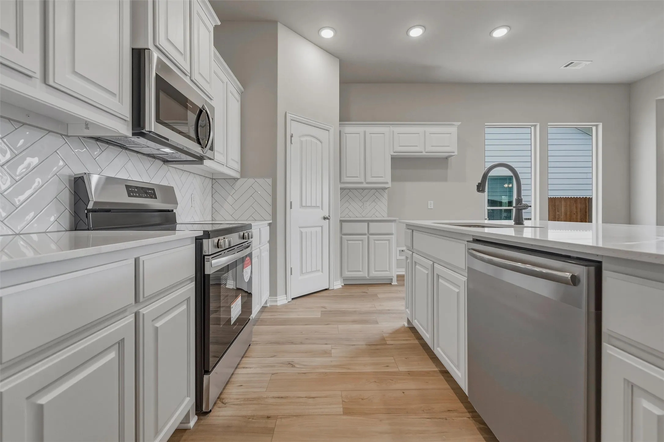 White cabinetry, light-toned countertops, stainless steel appliances, wood-finish flooring, and recessed lighting