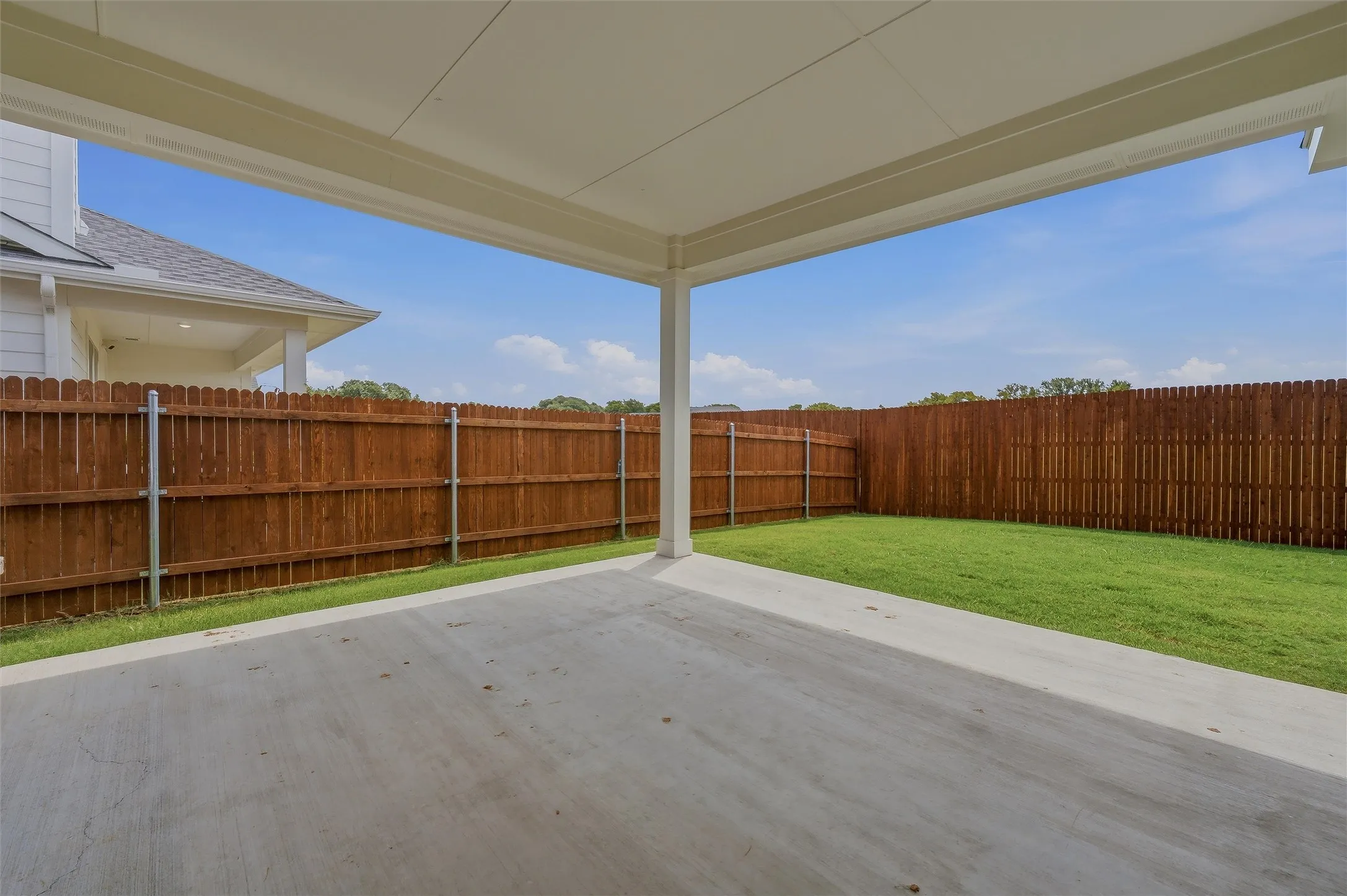Covered concrete patio with a spacious grass yard and wood privacy fencing