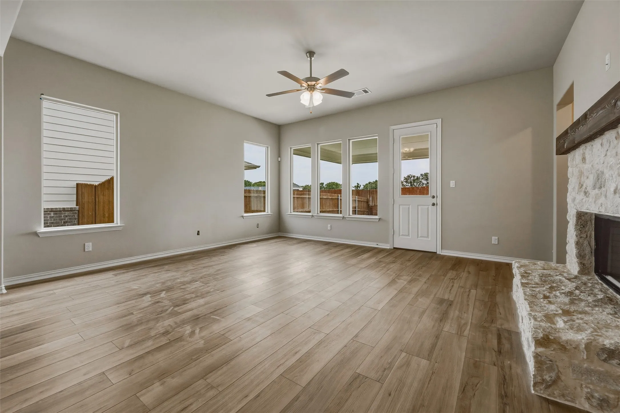 Vaulted ceiling, wood-finish flooring, stone-clad fireplace with mantel, multiple windows, and a ceiling fan with integrated lighting