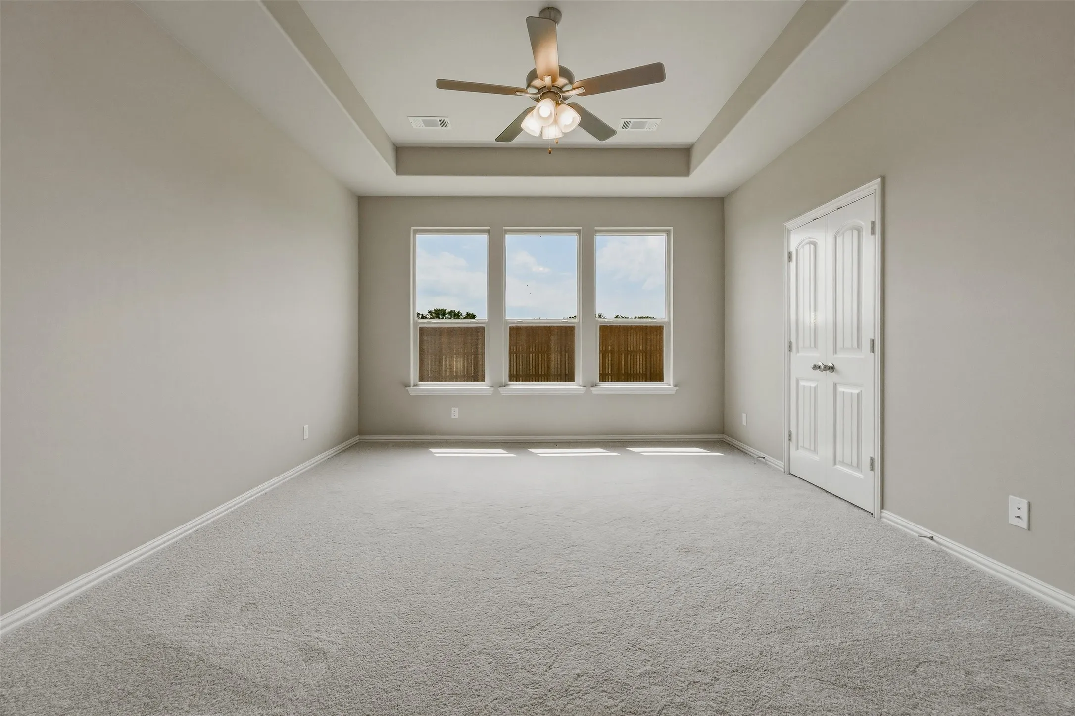 Recessed ceiling with a ceiling fan, three windows, light gray walls, and light gray carpet