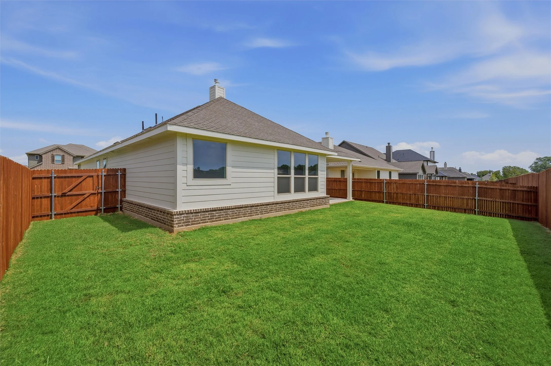 Expansive rear yard featuring green lawn, a wood privacy fence, and a gate