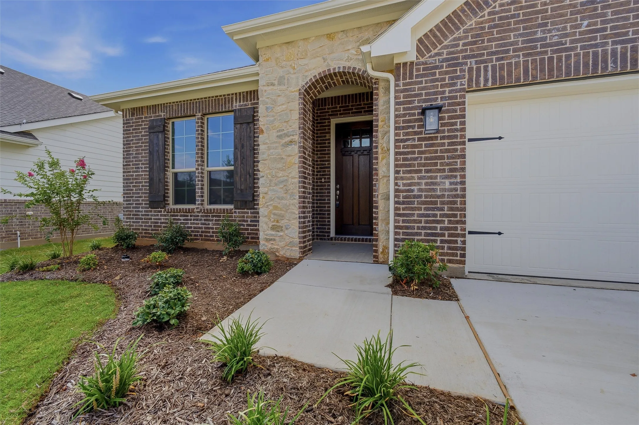 Brick exterior with stone accents, arched entryway, a dark wood-paneled door, and a two-car garage