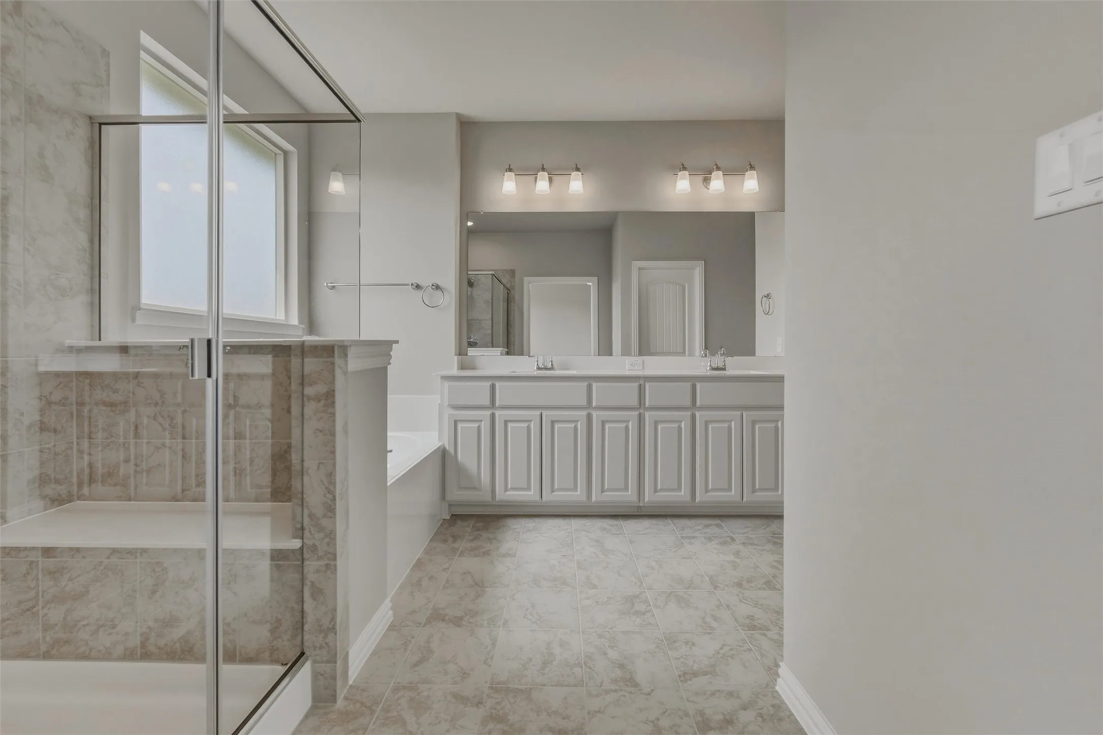 Spacious bathroom featuring a dual vanity, large mirror, tile flooring, and a walk-in shower with built-in seating