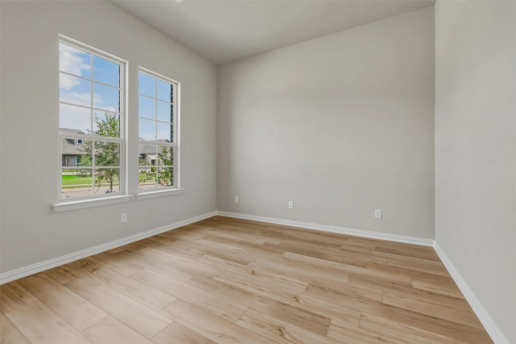 Spacious room featuring two tall windows with white trim, wood-finish flooring, and light-toned walls