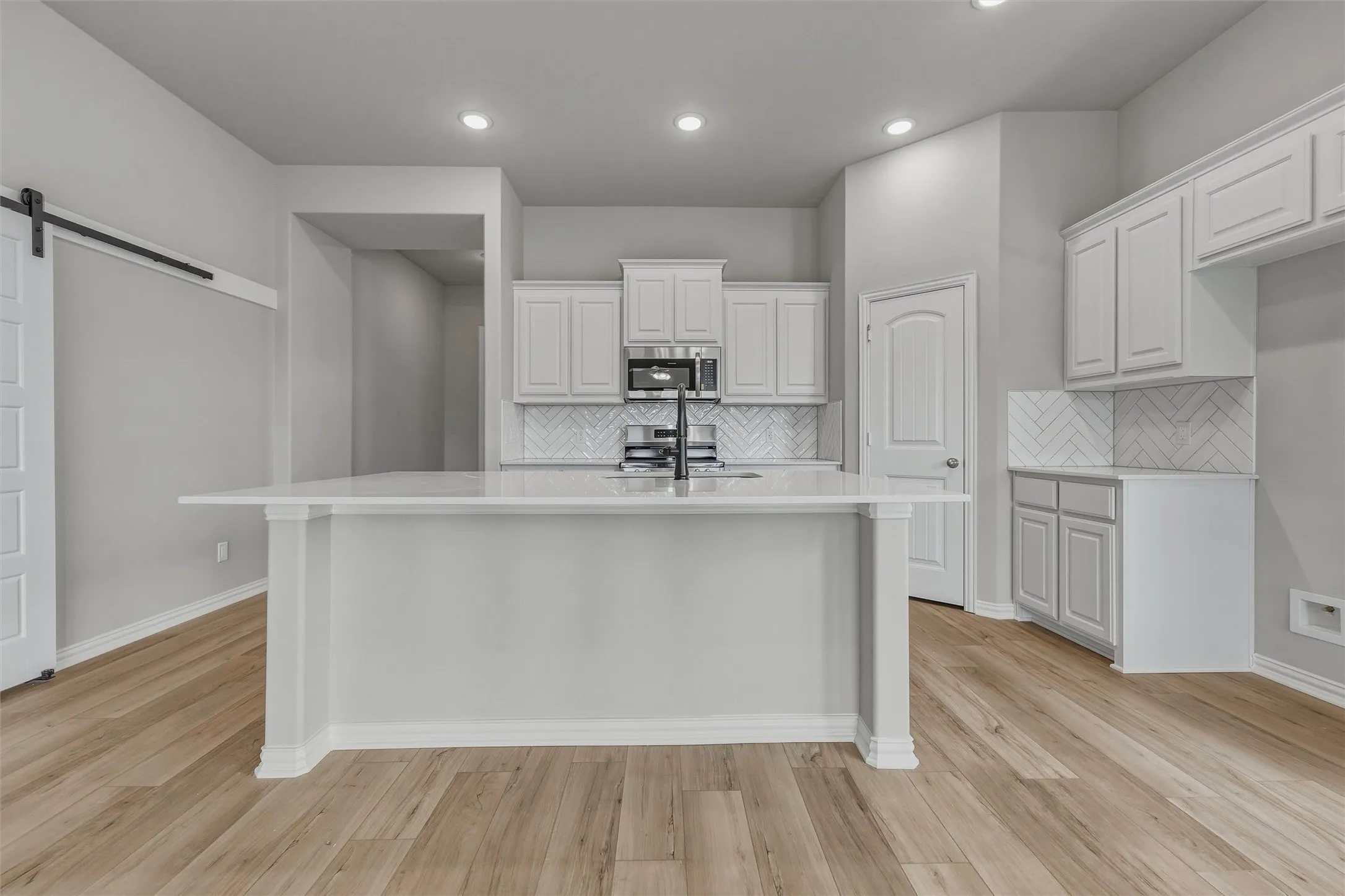 Kitchen featuring a central island with countertop, shaker-style cabinetry, a herringbone tile backsplash, integrated stainless steel appliances, and wood-finish flooring