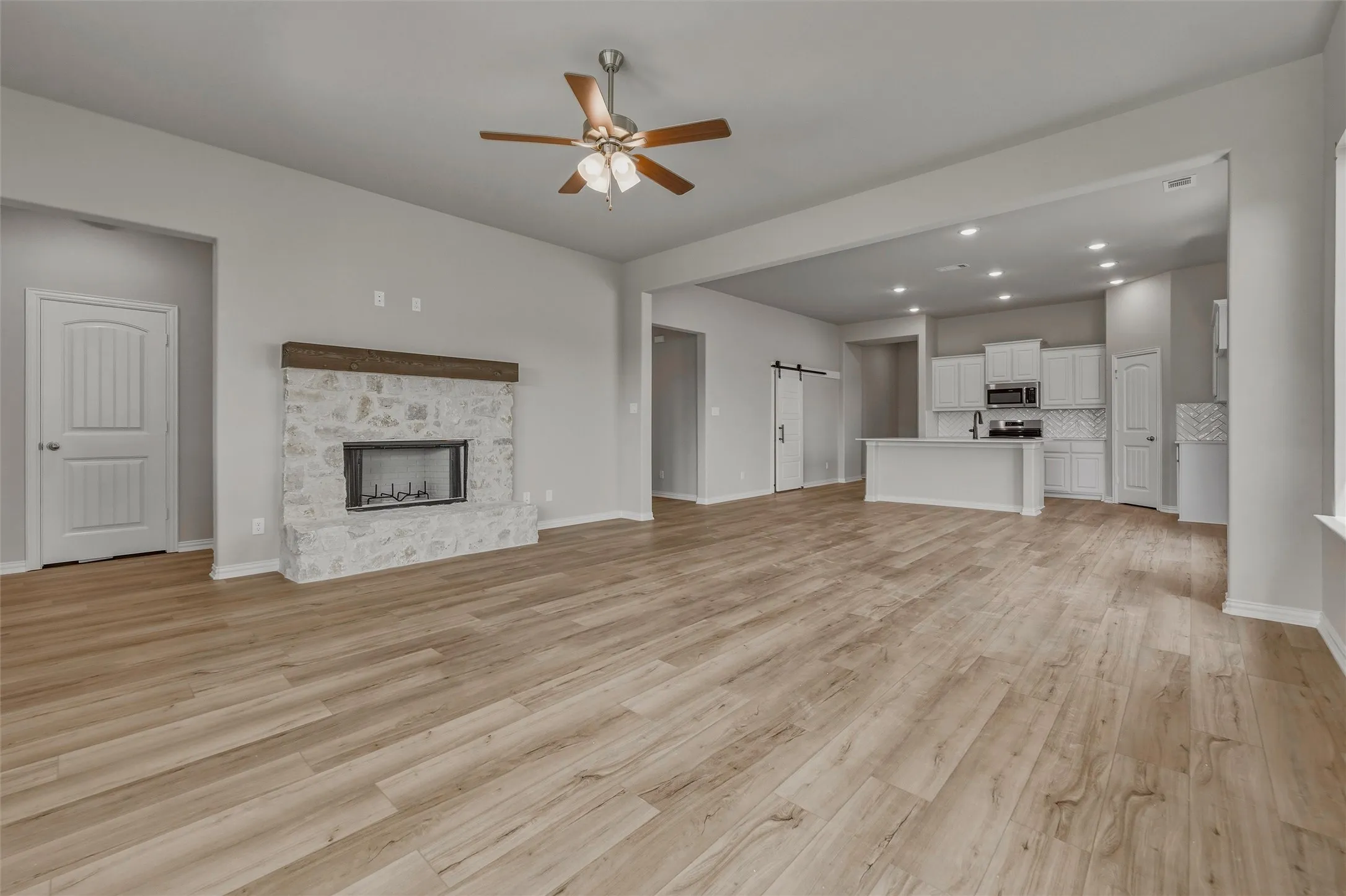 Spacious living area featuring wood-finish flooring, a stone fireplace with a substantial mantel, a ceiling fan, and recessed lighting