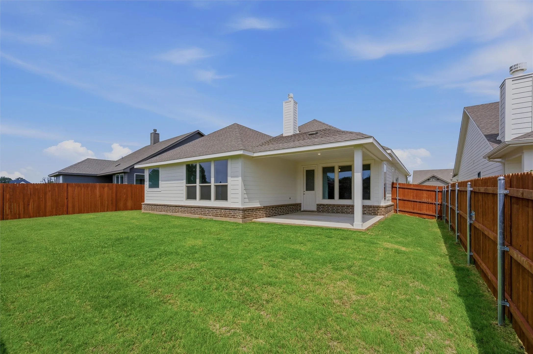 Expansive grassy yard with wood fencing, covered patio, white siding, and a stone facade