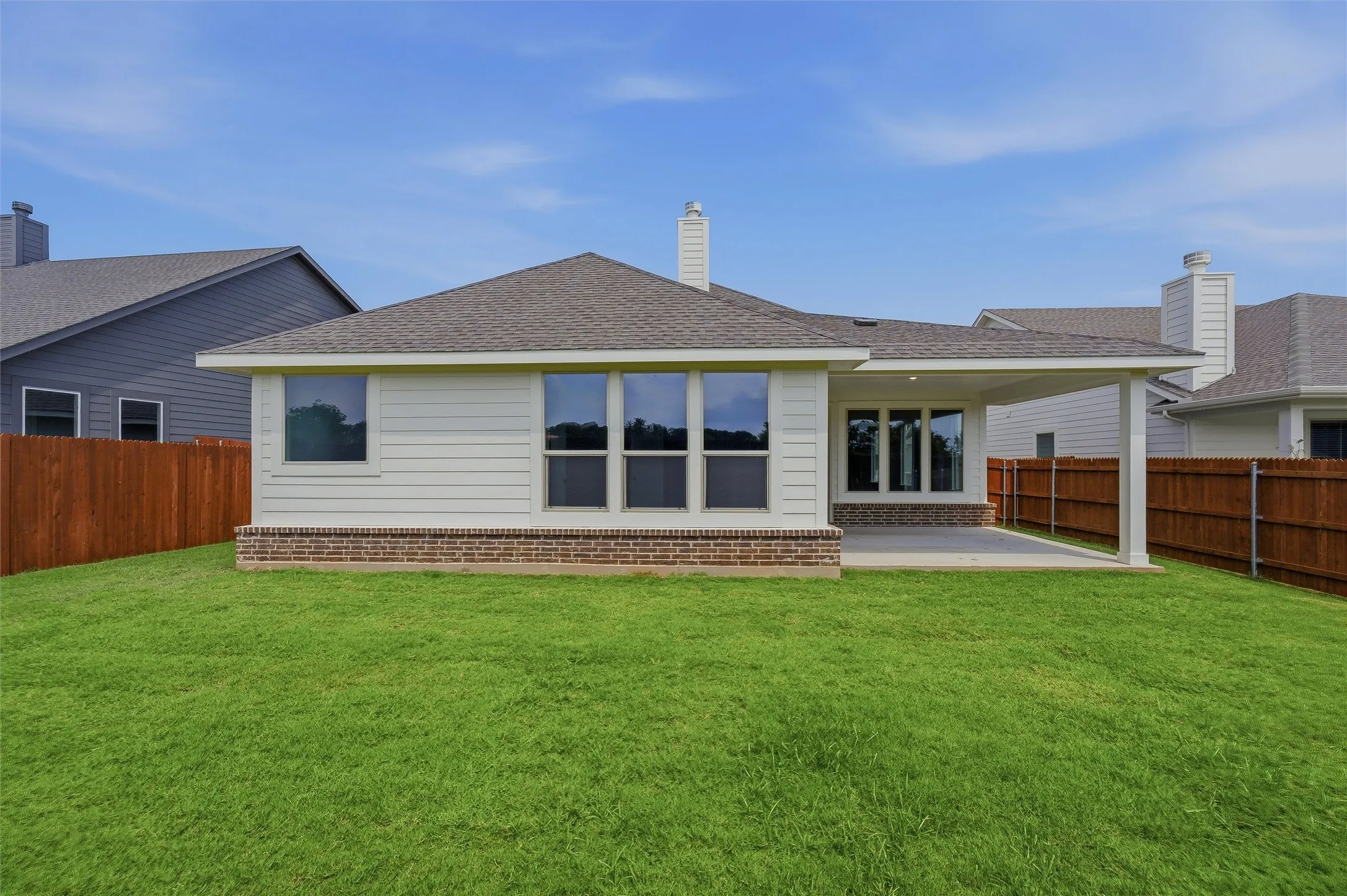 Expansive green lawn with a covered patio, white siding, brick detailing, and a dark shingle roof