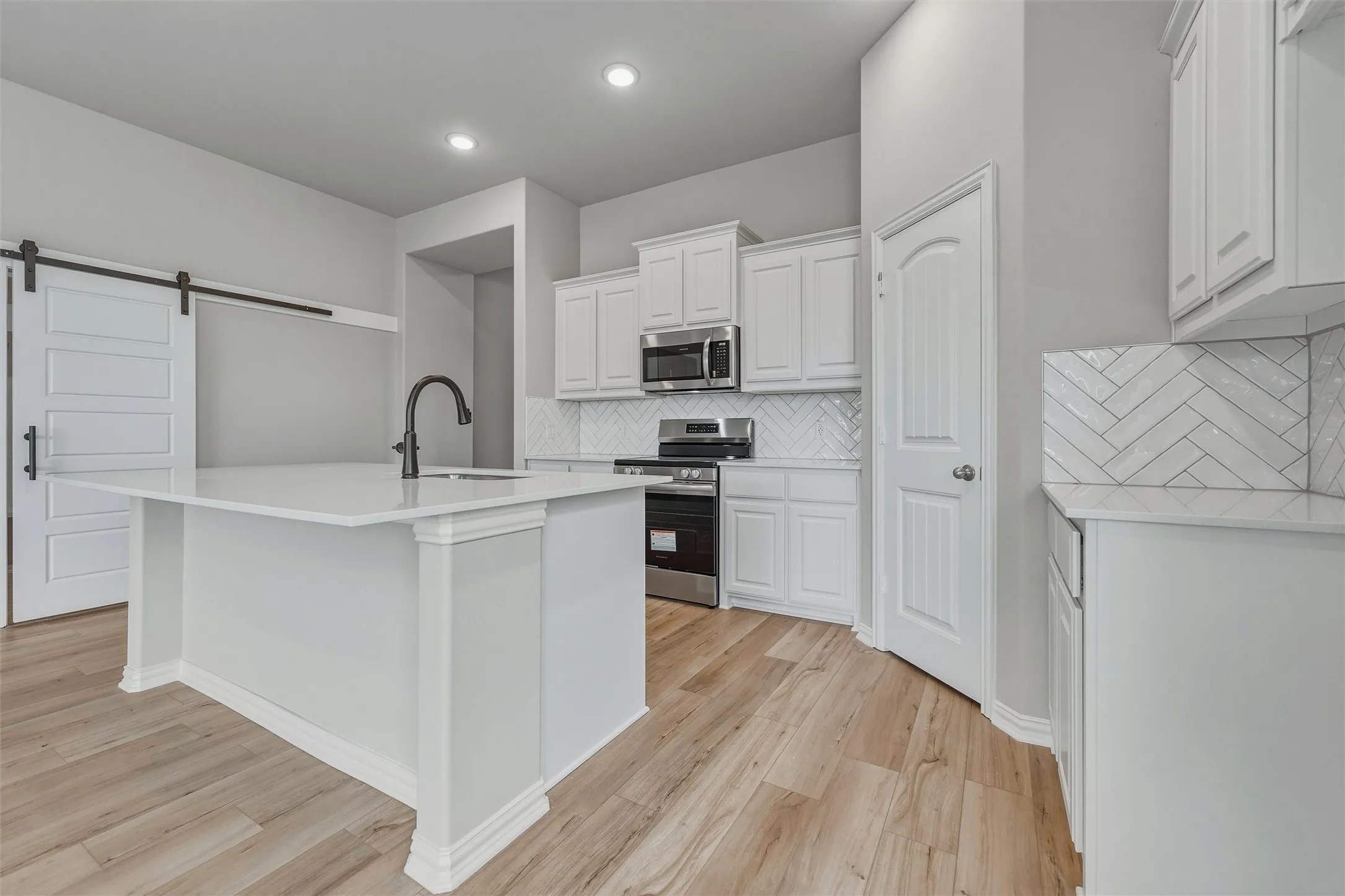 Kitchen featuring a central island with an undermount sink, white cabinetry, stainless steel appliances, herringbone tile backsplash, and wood-finish flooring