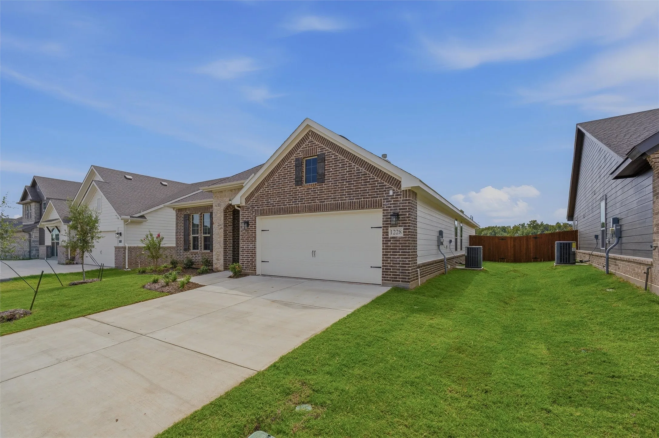 Brick and siding exterior with a concrete driveway, attached garage, and mature landscaping