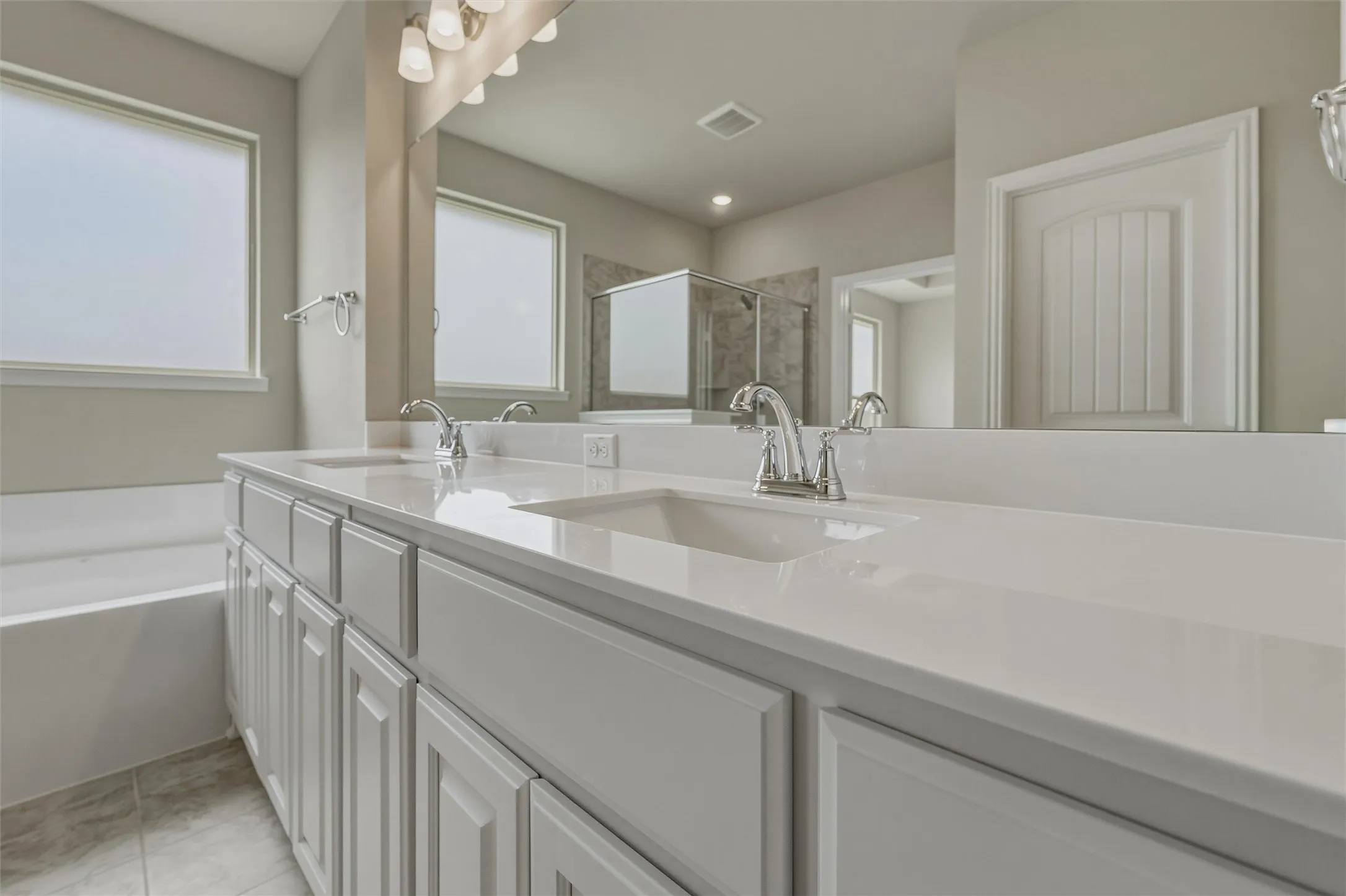 Dual vanity with white cabinetry, integrated sinks, chrome fixtures, and a large wall mirror