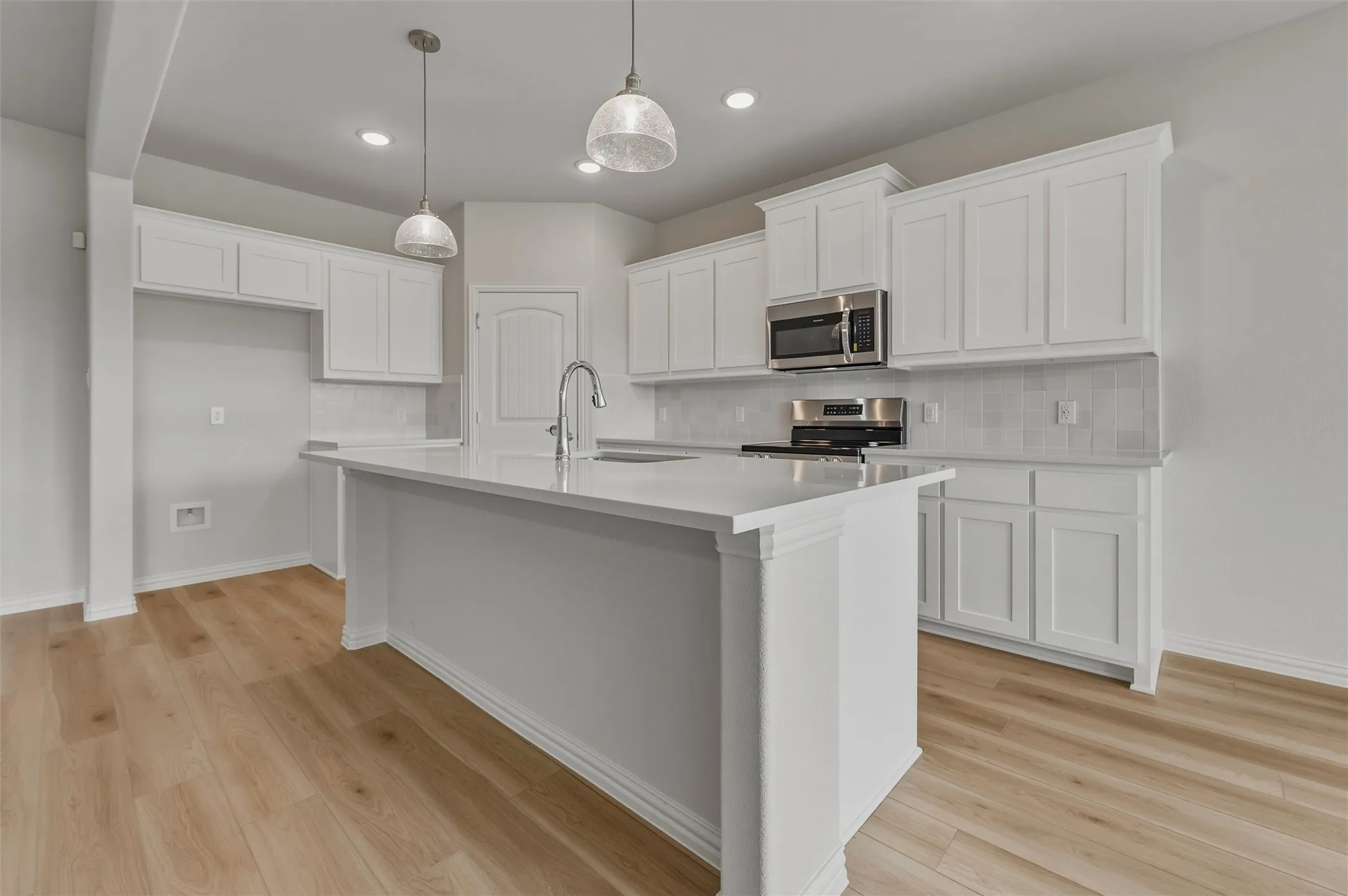 Modern kitchen featuring a central island, white cabinetry, integrated stainless steel appliances, and wood-finish flooring