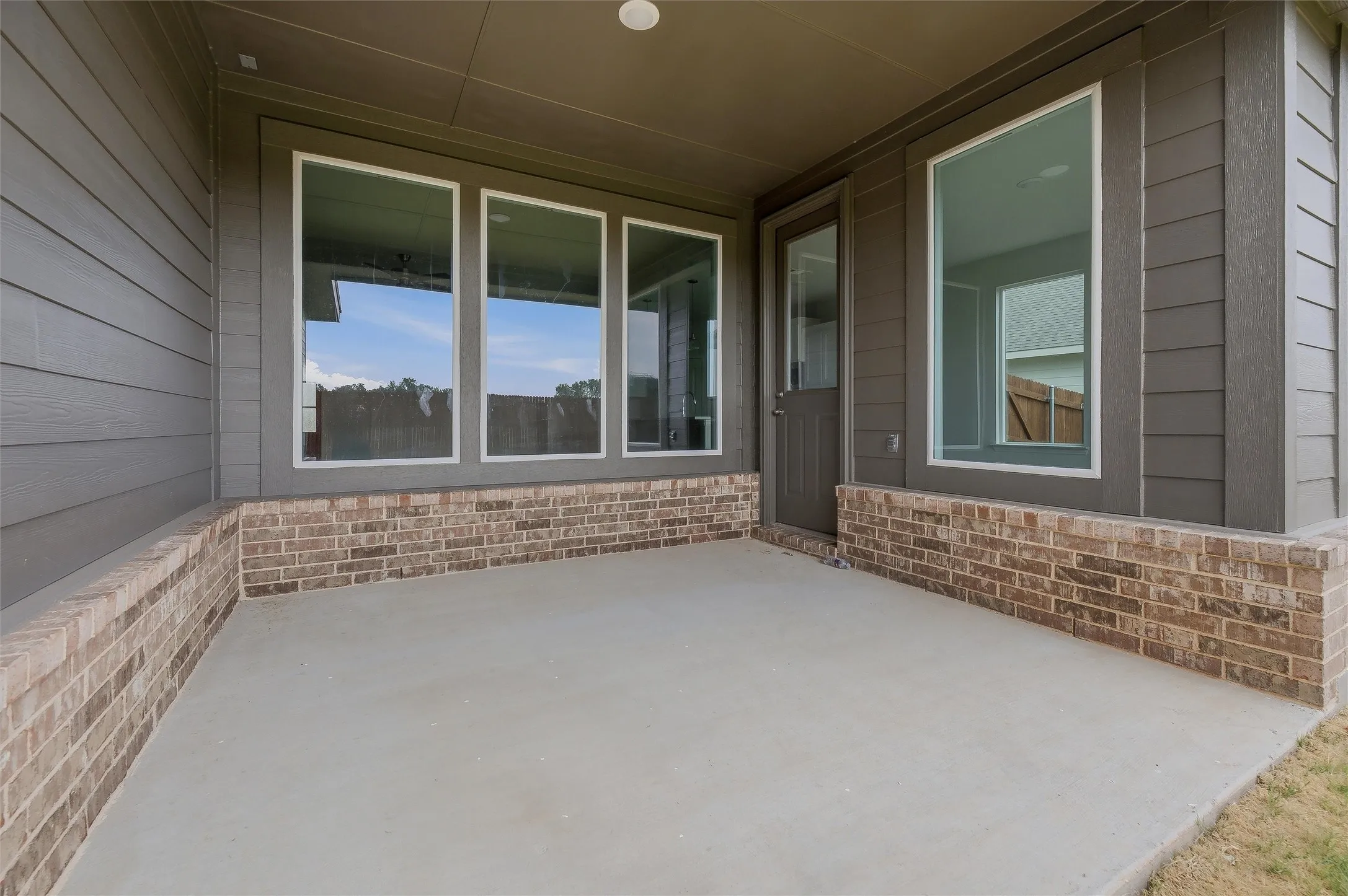 Covered concrete patio featuring a brick base and durable siding