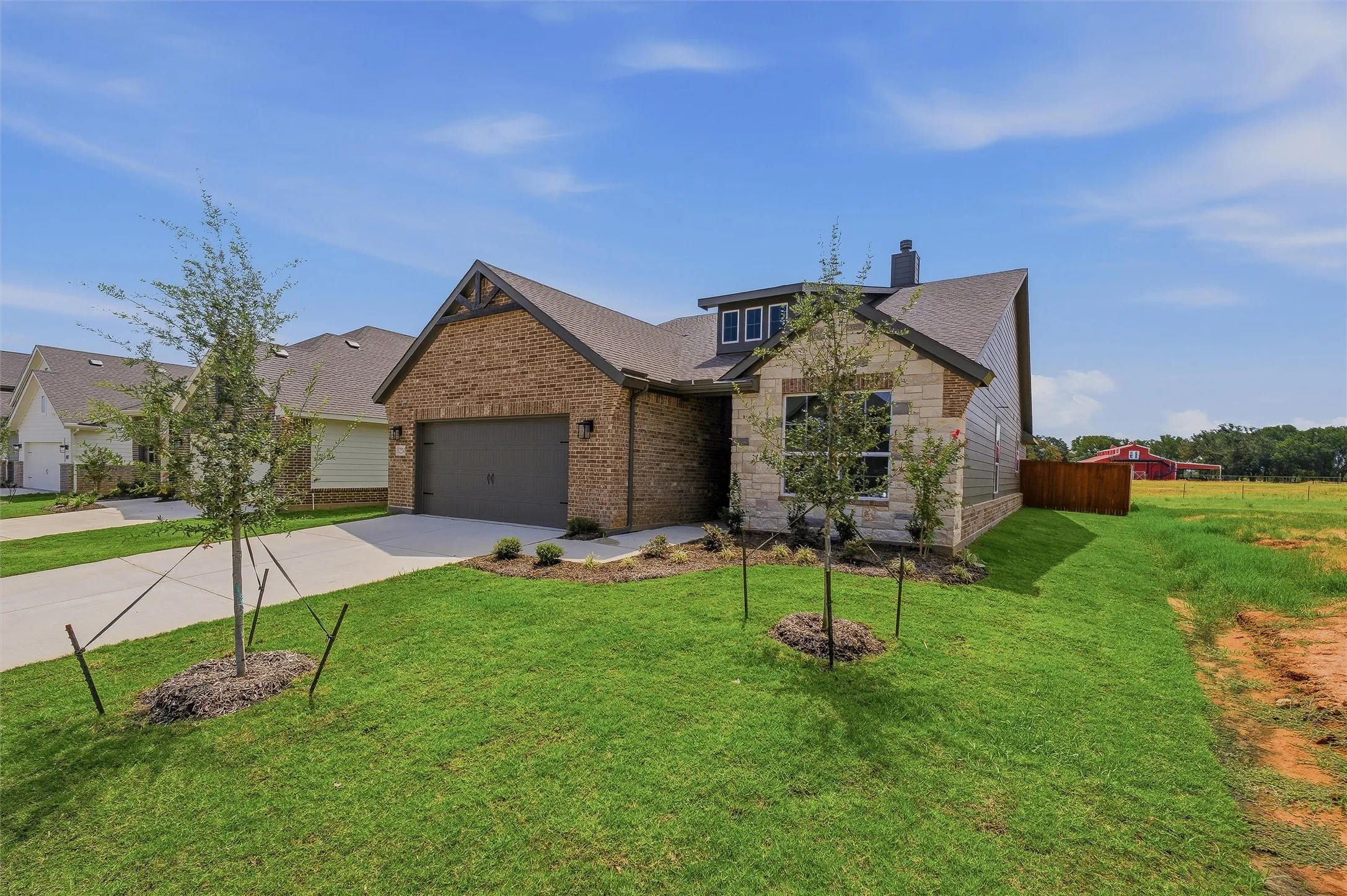 Brick and stone facade, attached garage, gabled roofline, front landscaping, and a wooden fence