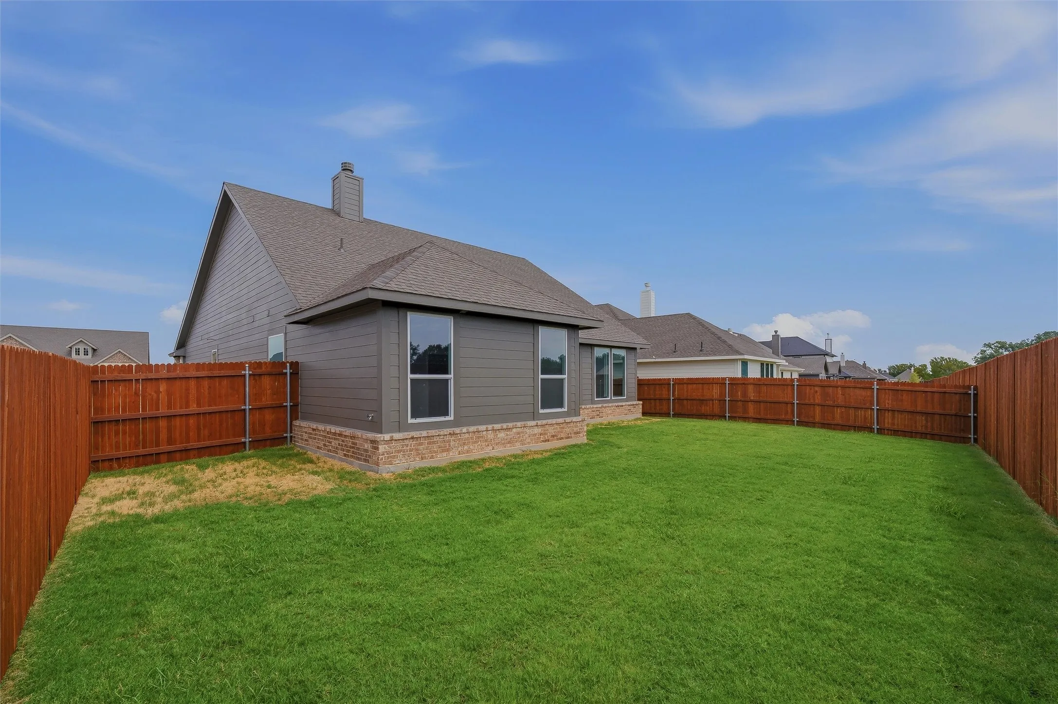 Expansive fenced backyard featuring a manicured lawn, brick and siding exterior, and multiple windows