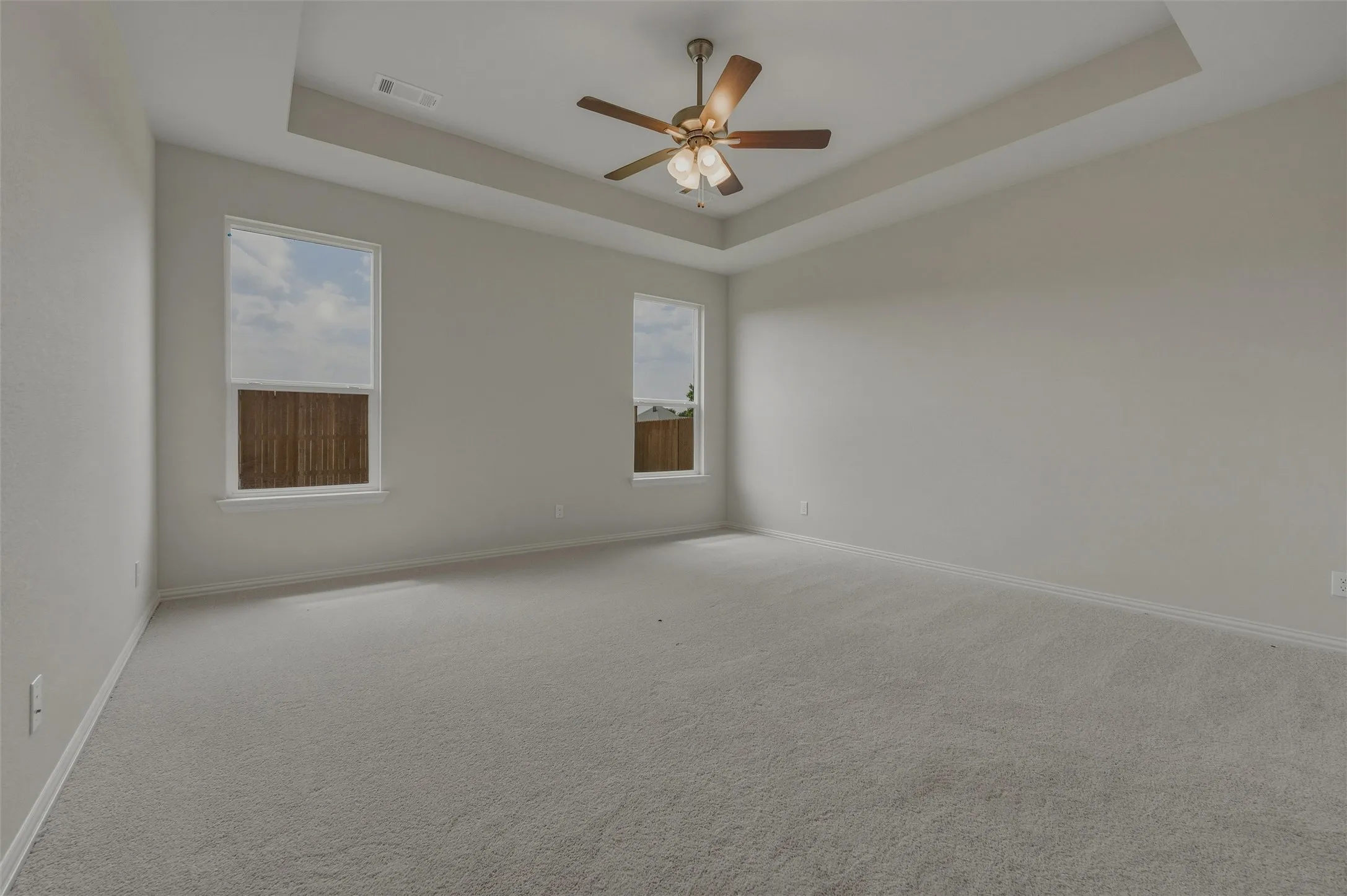 Tray ceiling with a ceiling fan, two windows, and light gray wall paint