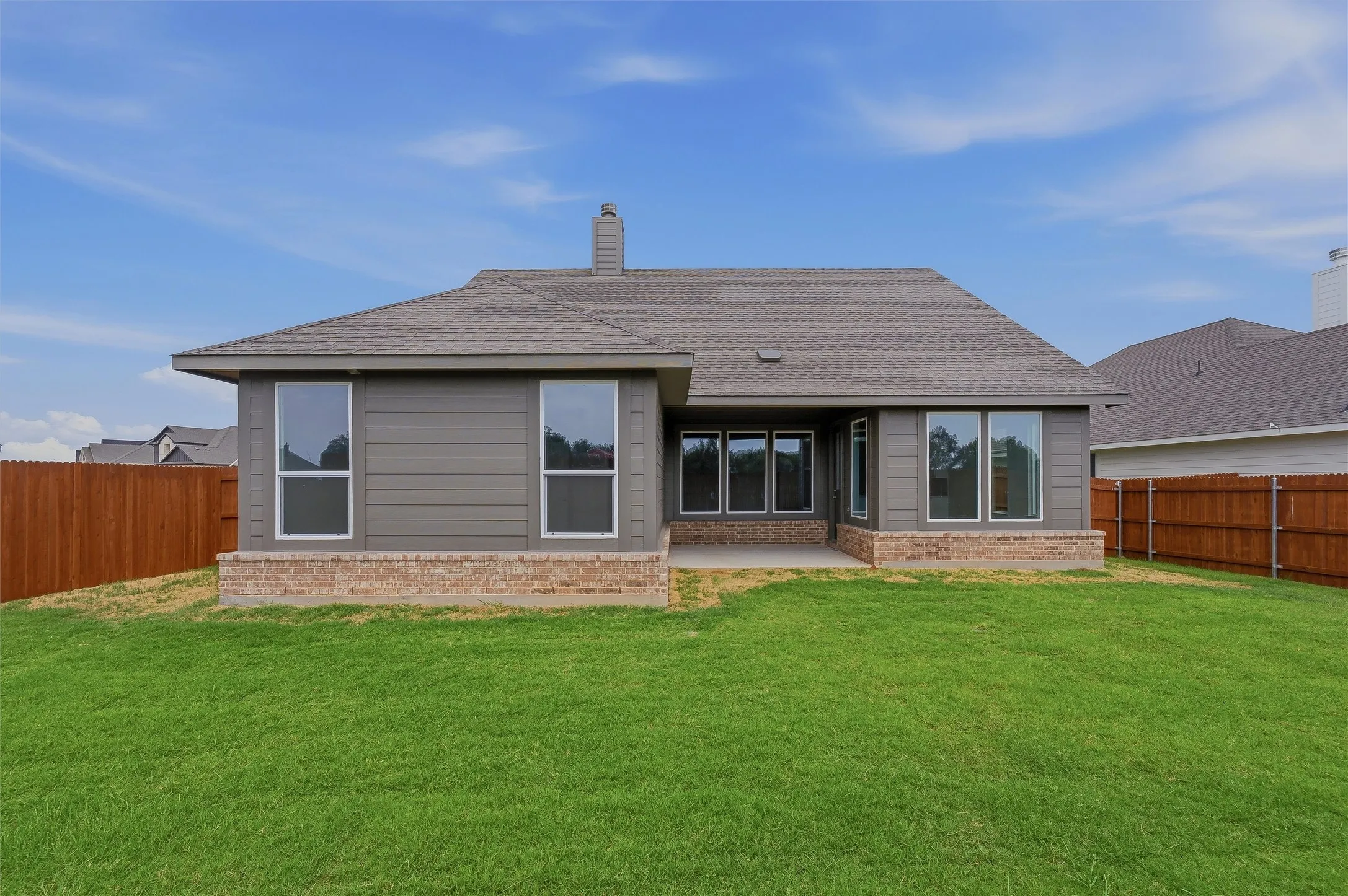 Expansive lawn area, architectural shingles, exterior siding, brick detailing, and a concrete patio