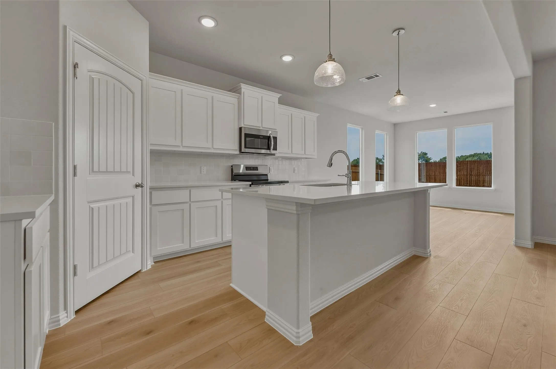 Kitchen featuring white shaker cabinetry, stainless steel appliances, a center island with sink, and wood-finish flooring