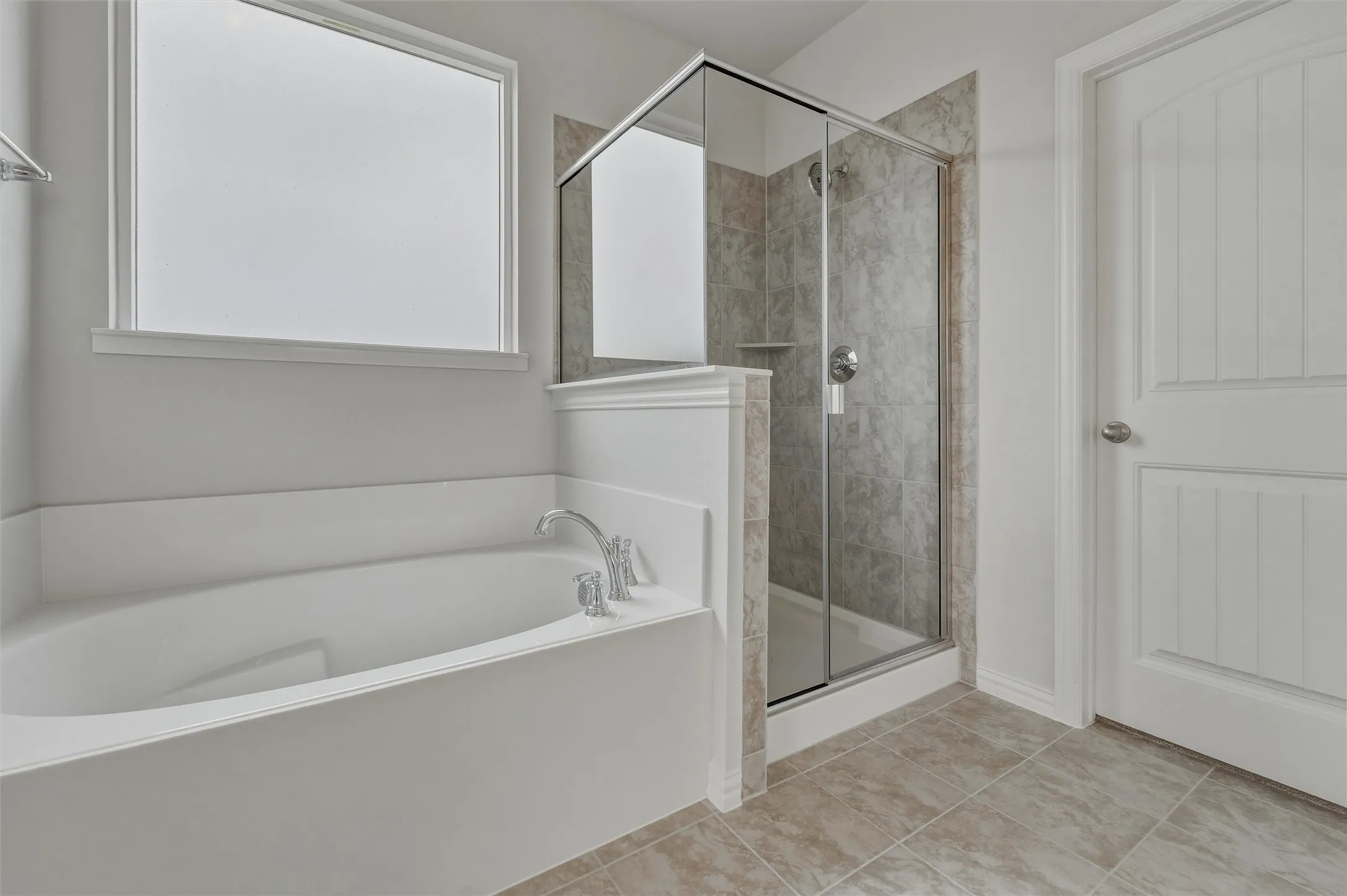 Soaking tub with chrome fixtures, glass-enclosed shower with tiled surround, and large format tile flooring