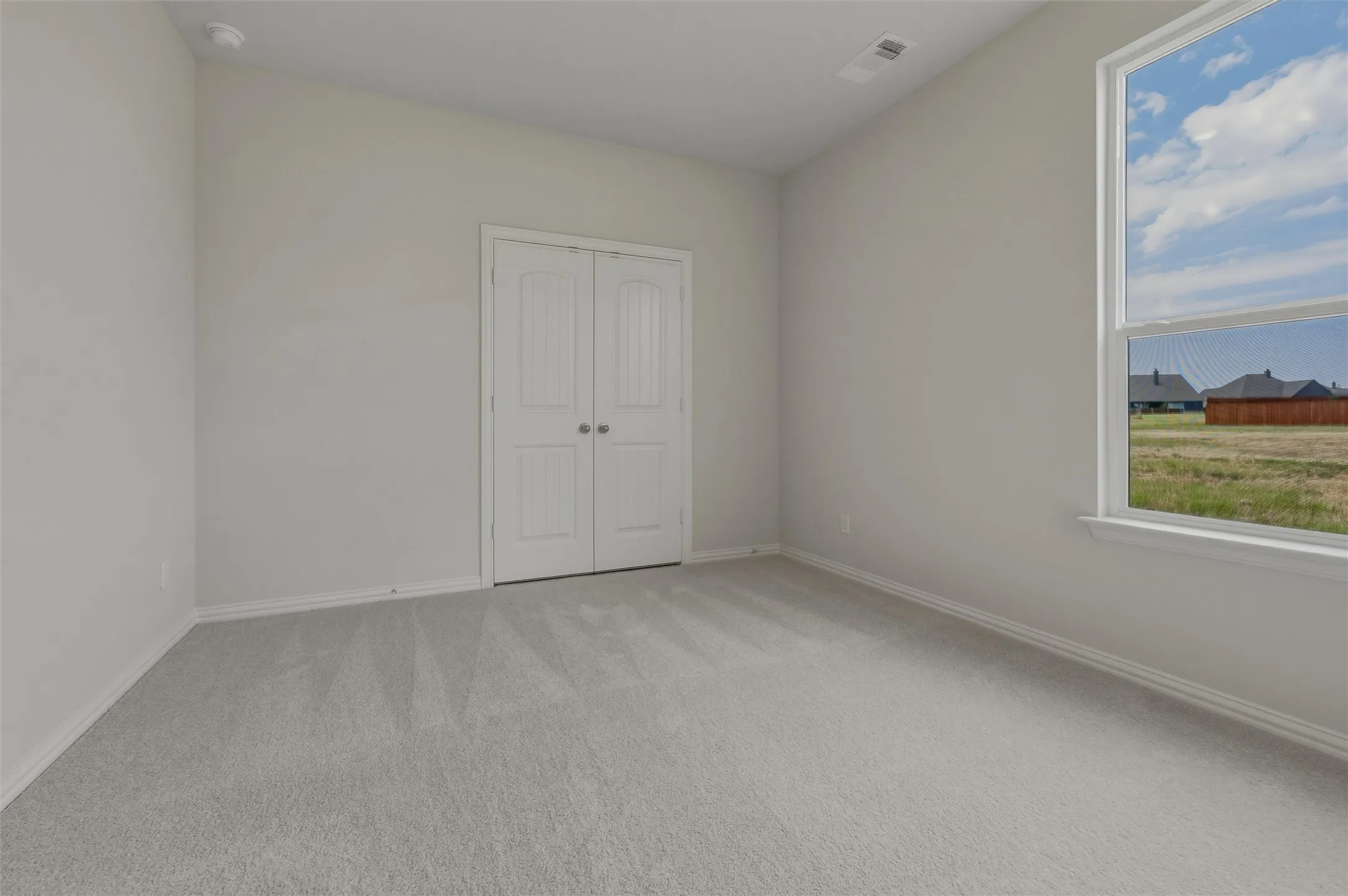 Soft gray carpeting throughout, white painted walls, white double-door closet with round pulls, and a large window with white trim