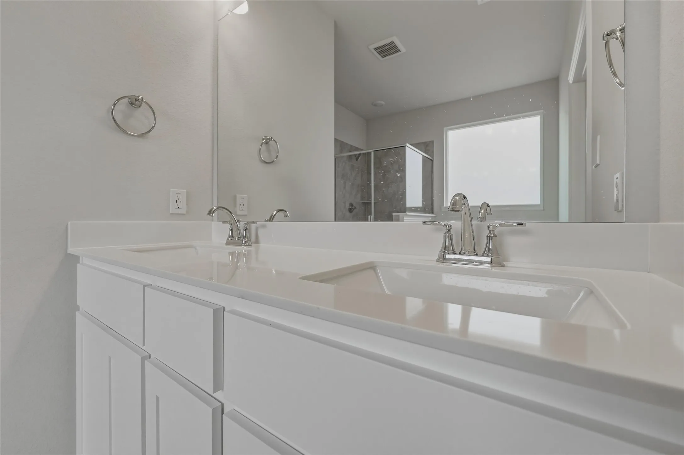 Dual vanity with integrated sinks, white cabinetry, polished chrome fixtures, and a large mirror